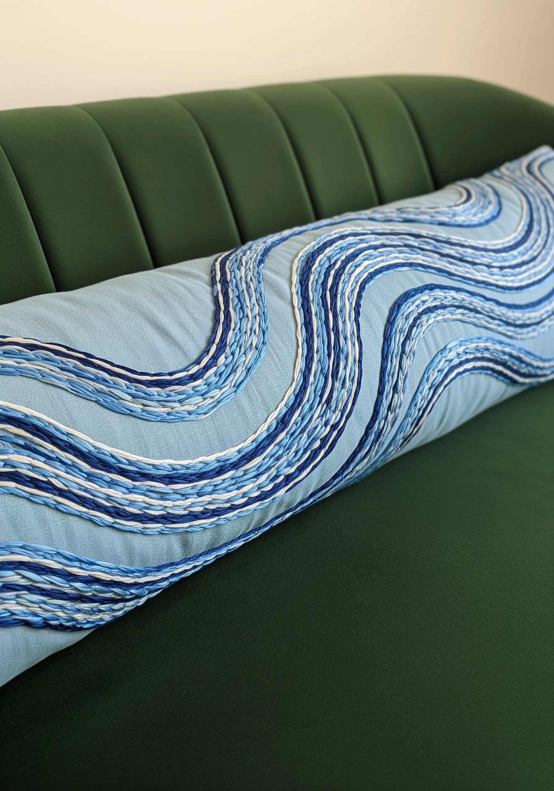 A long blue pillow with wavy, horizontal lines made from couched blue and white cords.