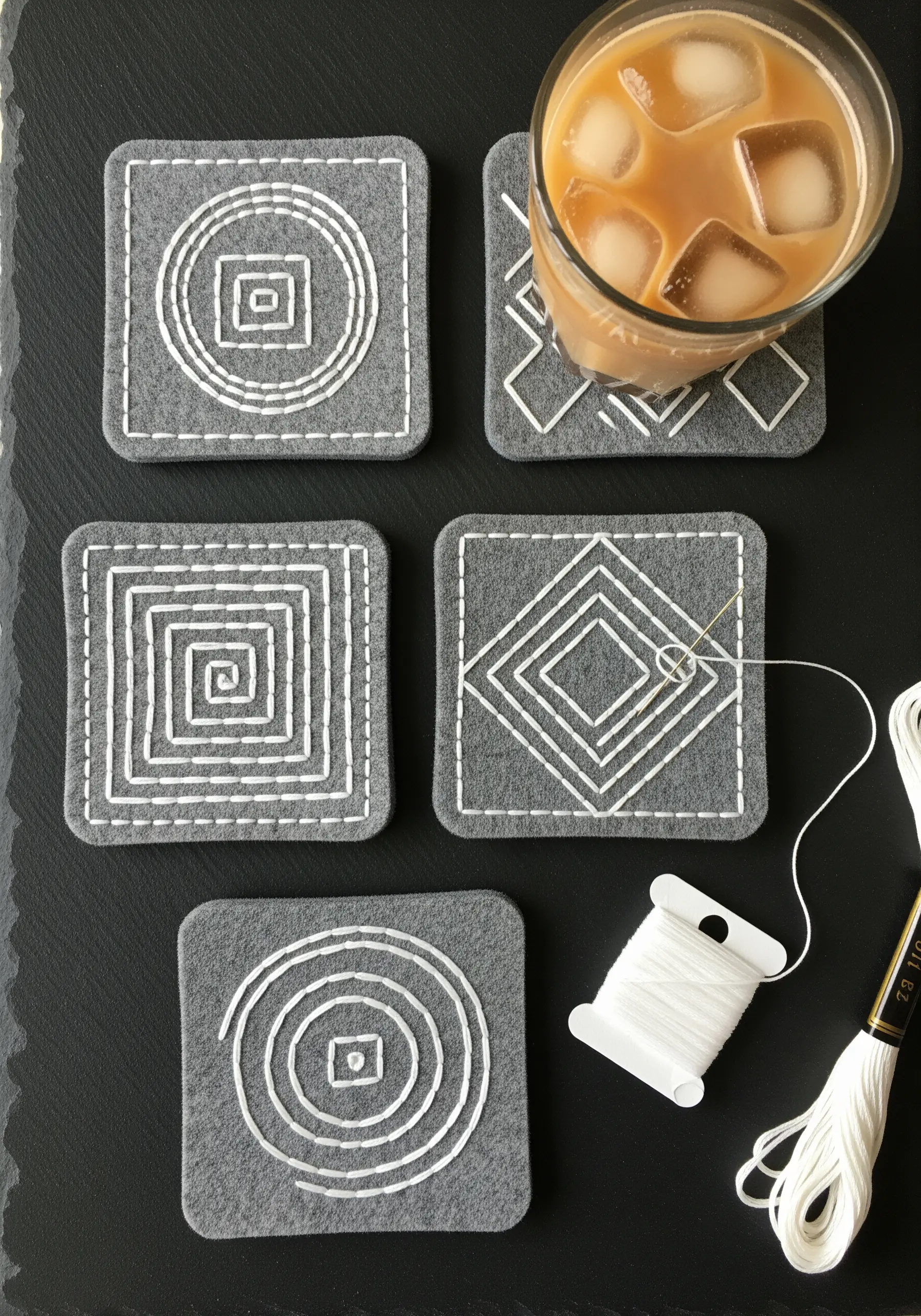 A set of grey felt coasters with minimalist geometric patterns in white thread