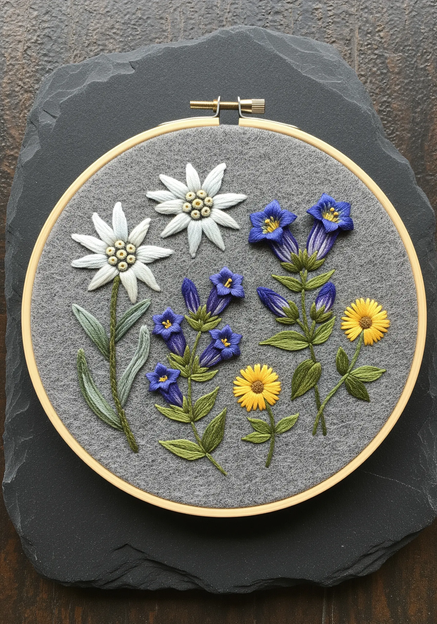 Embroidery of alpine flowers, including edelweiss and gentian, on a grey wool felt background.