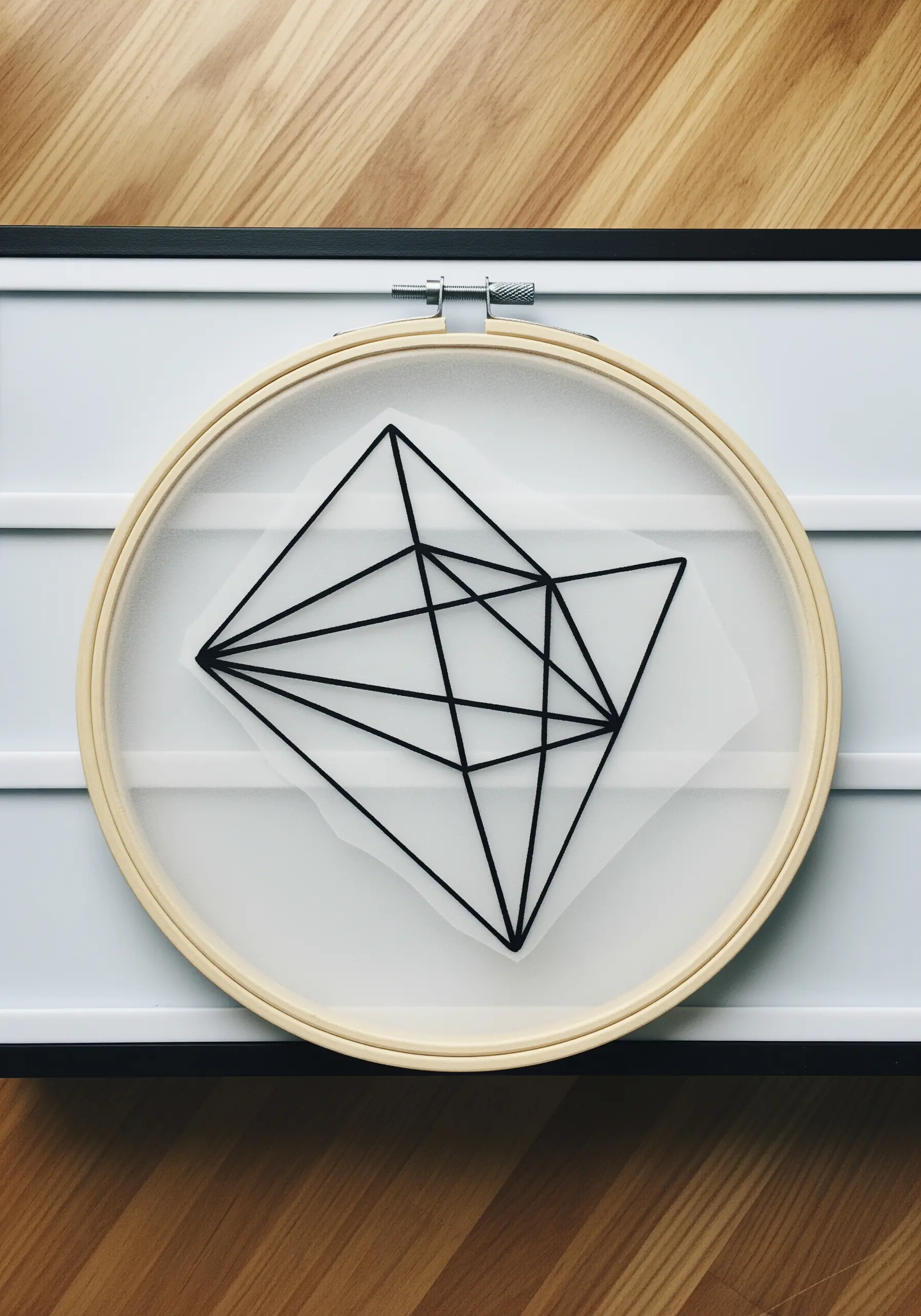 A black geometric line design embroidered directly onto translucent vellum paper inside a hoop.