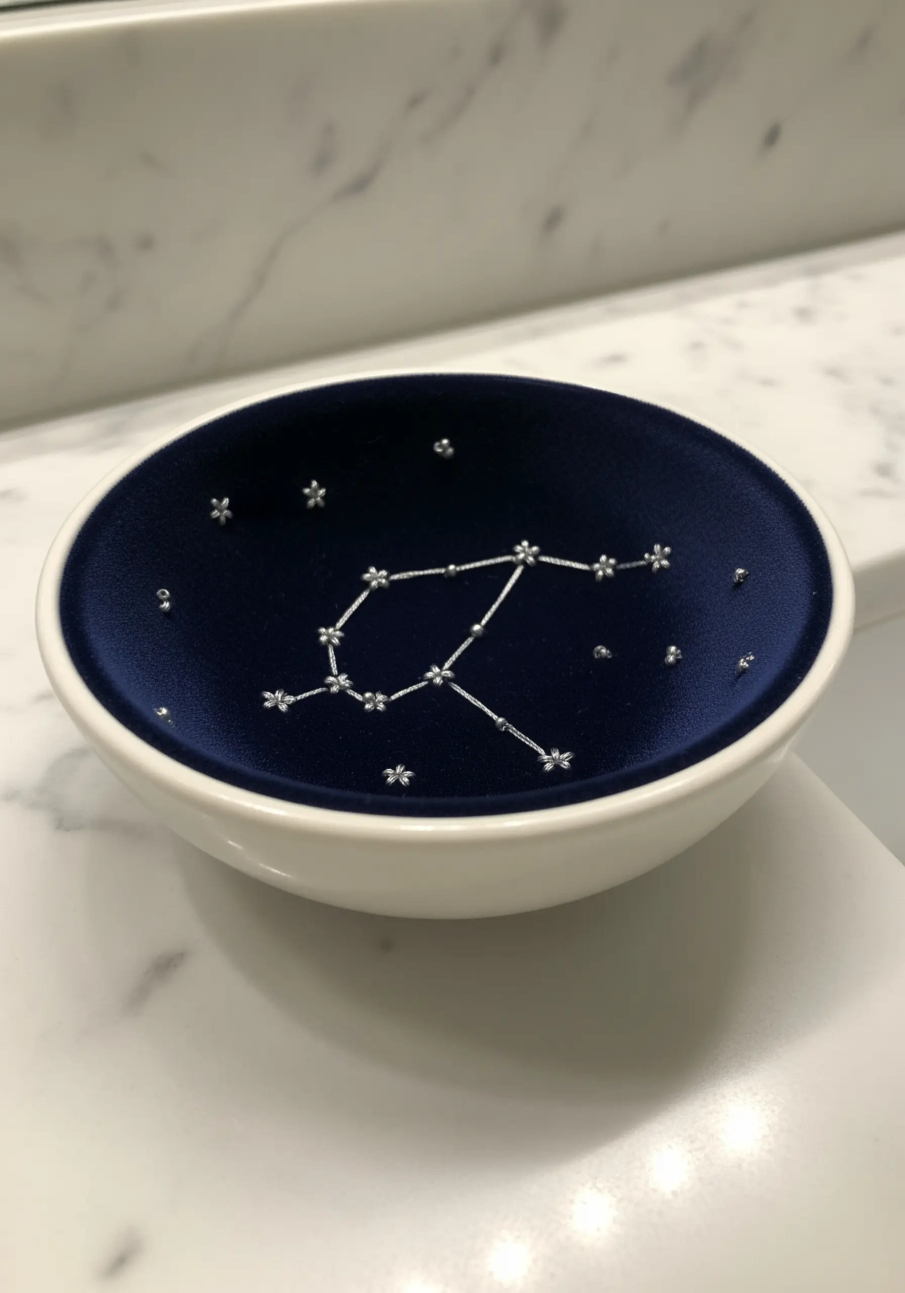 A constellation stitched with silver thread and beads on a navy velvet-lined trinket dish.