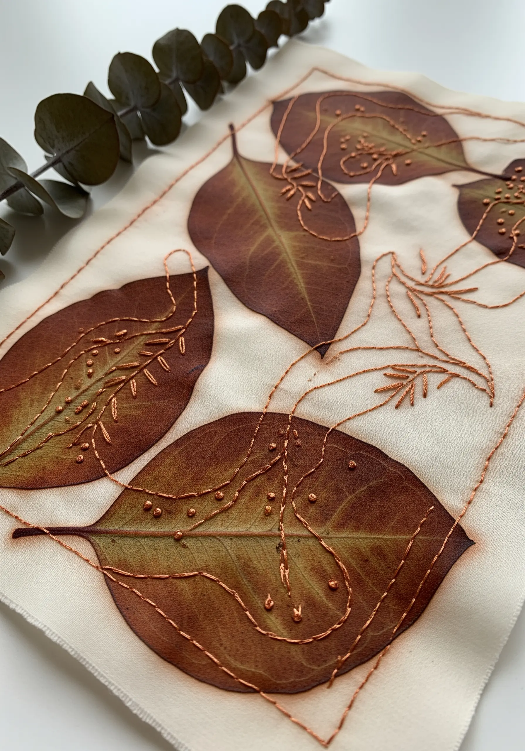 Fabric printed with the faint brown shapes of real leaves, embellished with copper-colored embroidery.