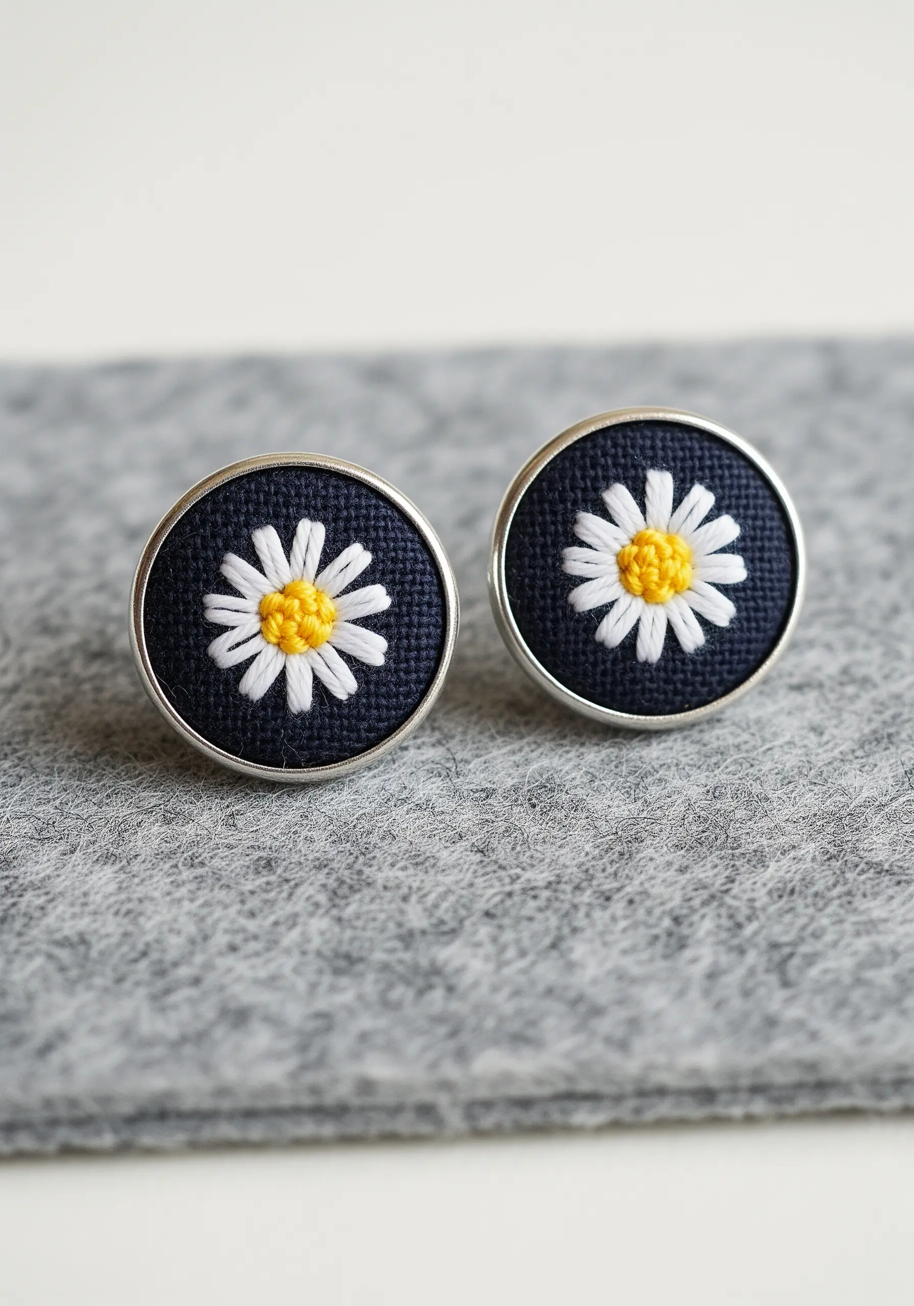 A pair of embroidered cufflinks with tiny white daisies on a navy blue fabric background.