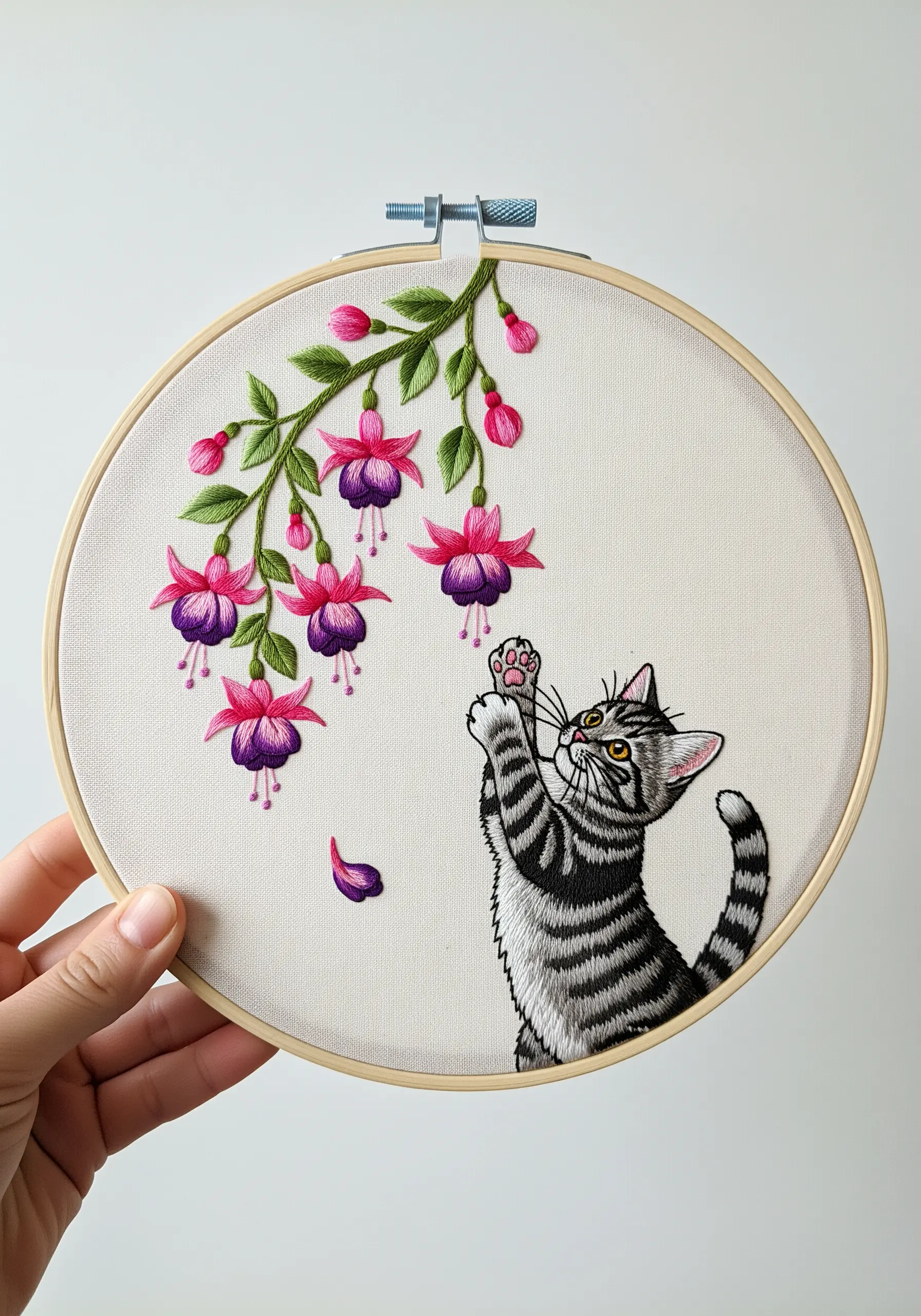 Embroidered tabby kitten reaching for dangling fuchsia flowers.