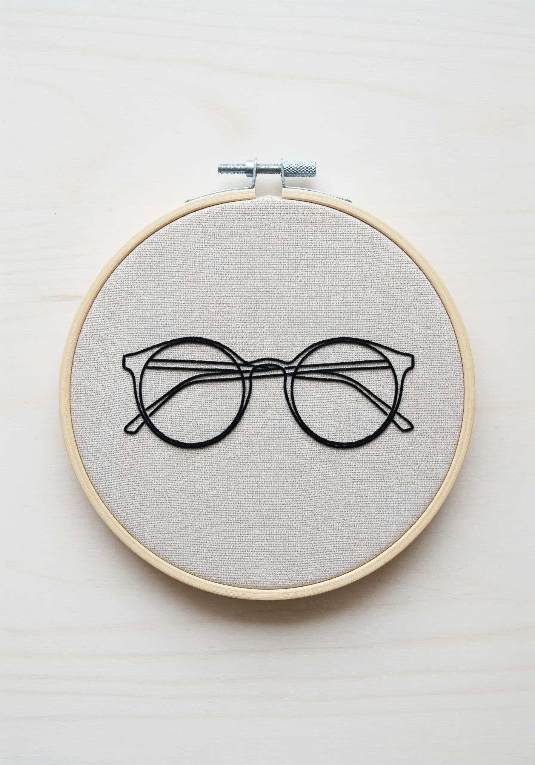 A pair of glasses embroidered in a clean, black, single-line style on grey fabric.