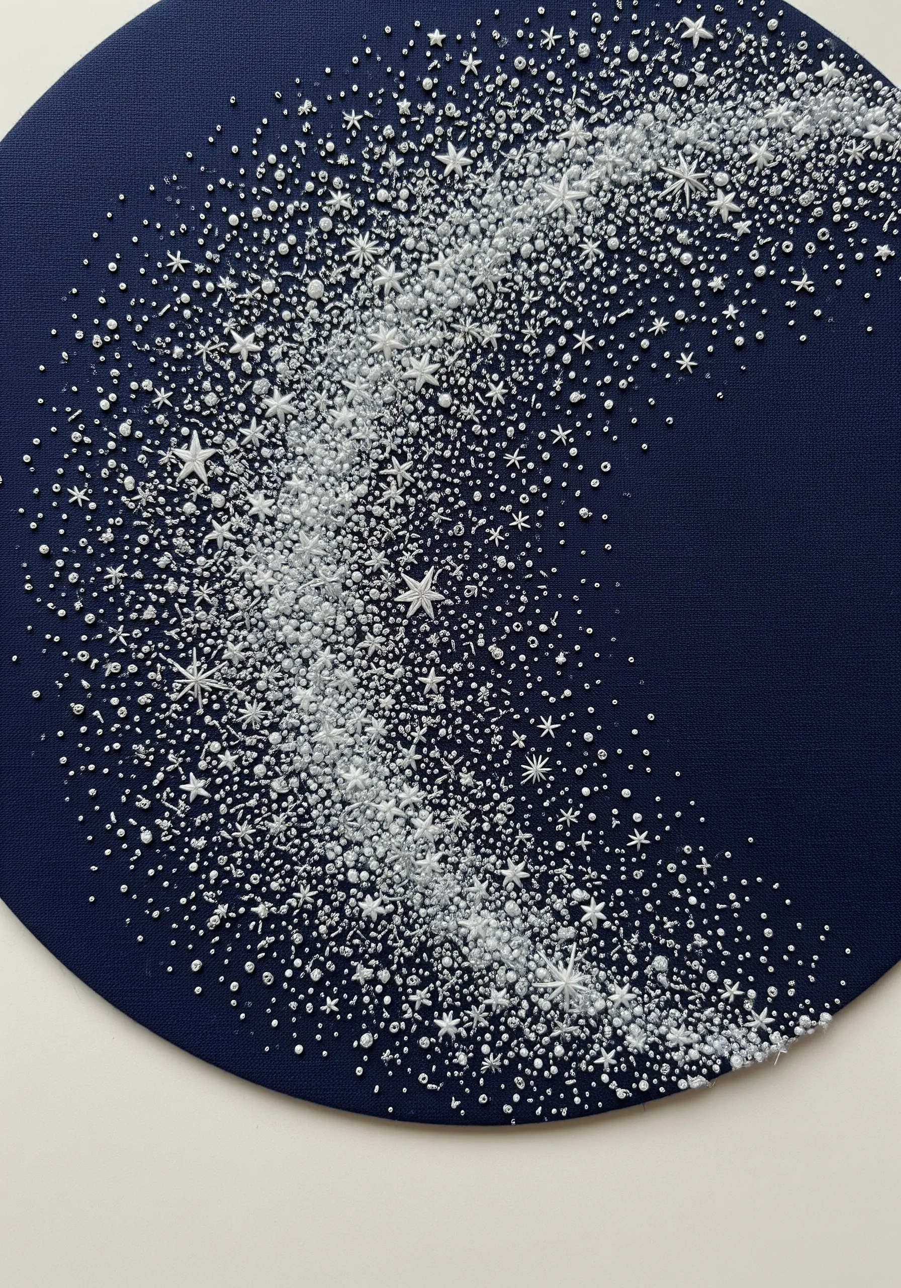Abstract embroidery of the Milky Way using white and silver beads on dark blue fabric.