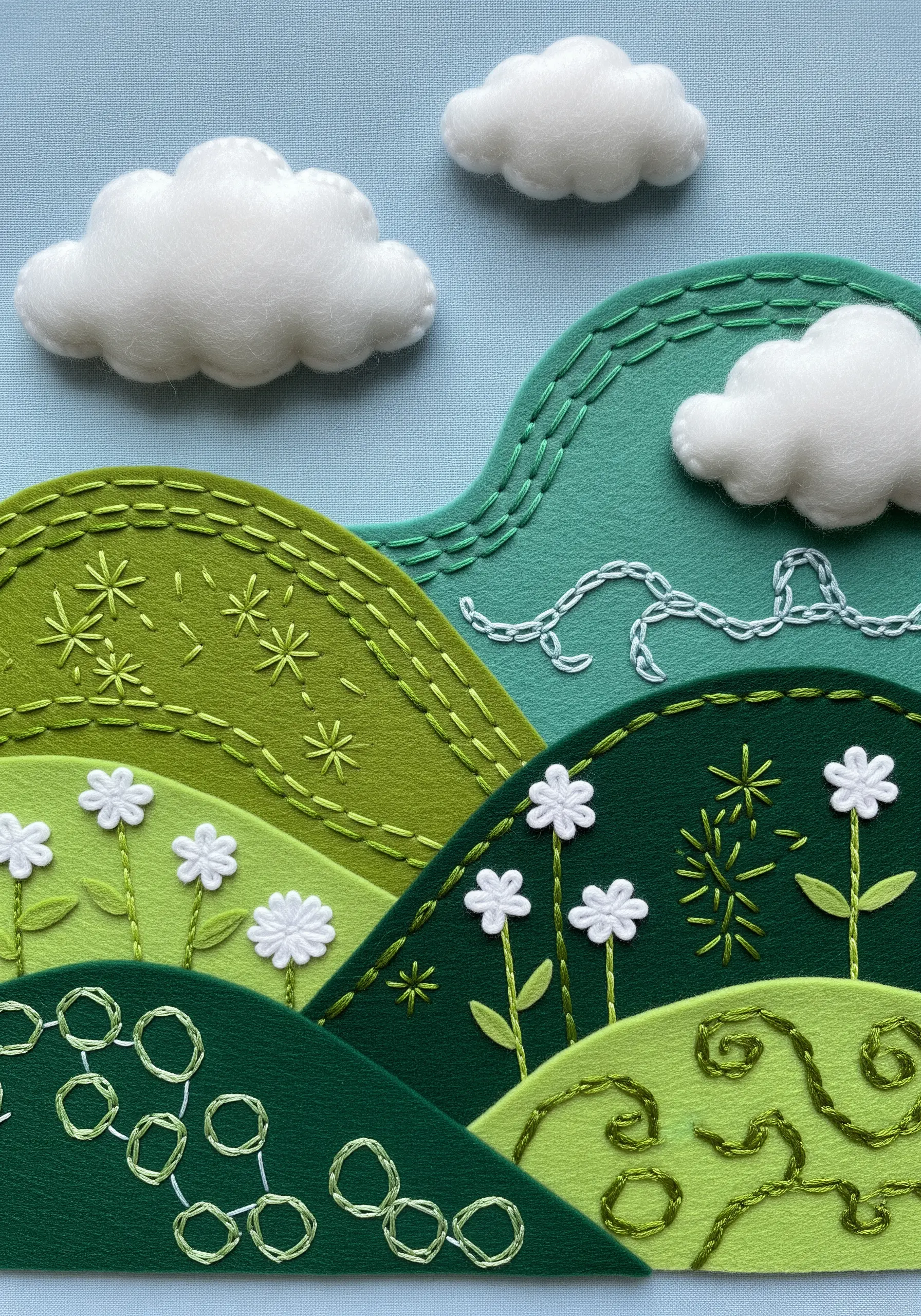 Layered felt landscape with decorative embroidery stitches creating hills and flowers.