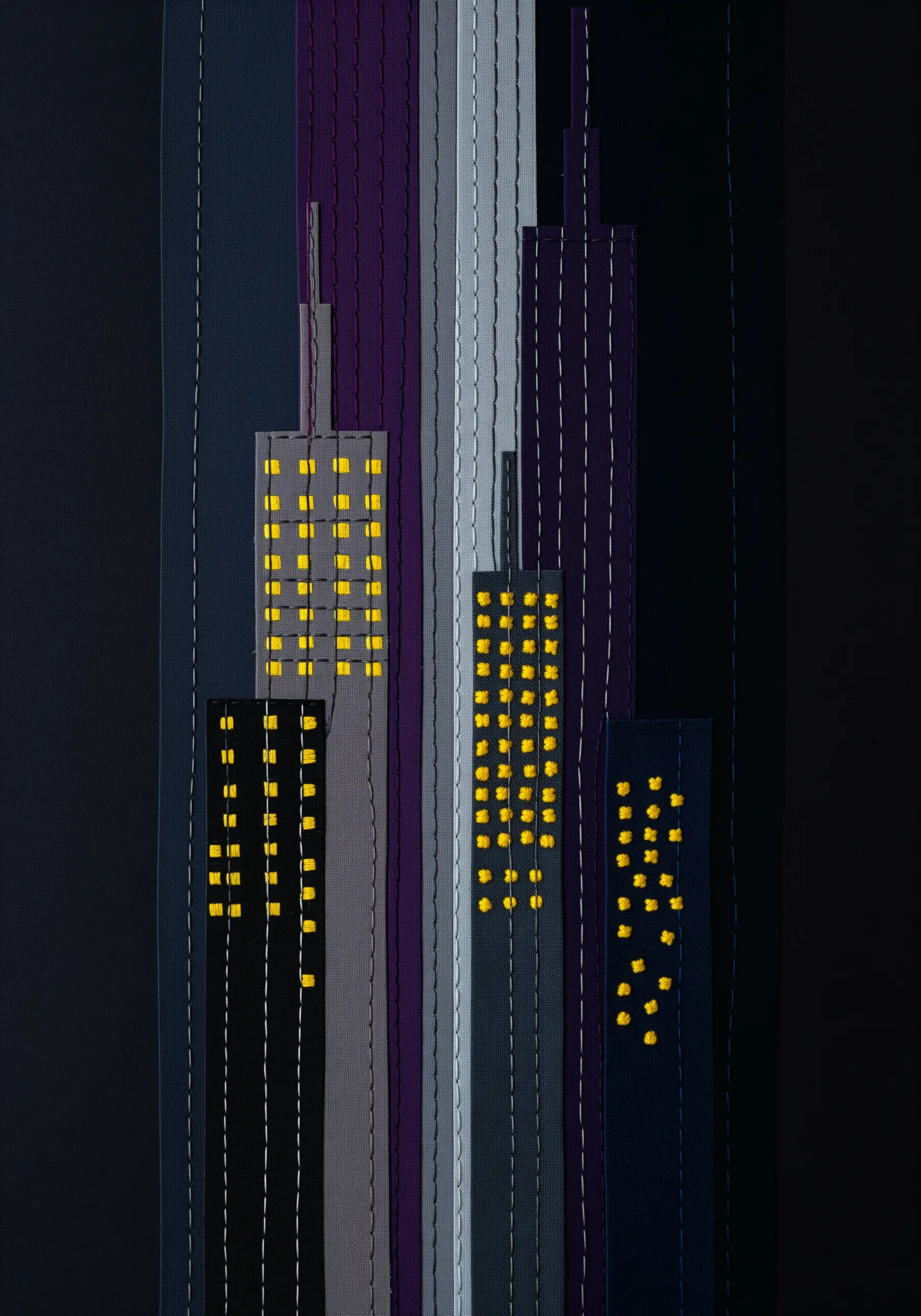 An abstract cityscape made from vertical fabric strips in dark colors, with yellow stitches for windows.