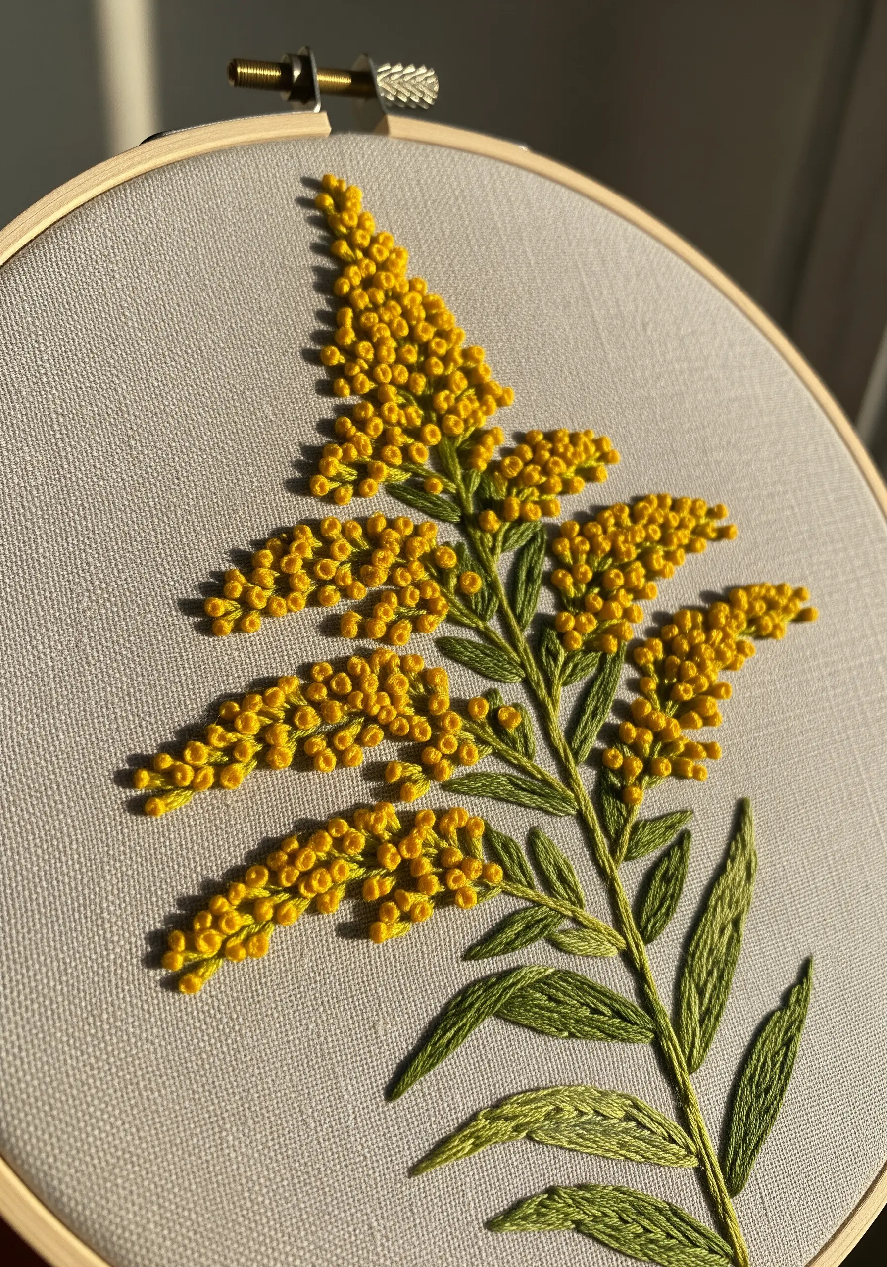 Yellow goldenrod embroidery using dense clusters of colonial knots on gray fabric.