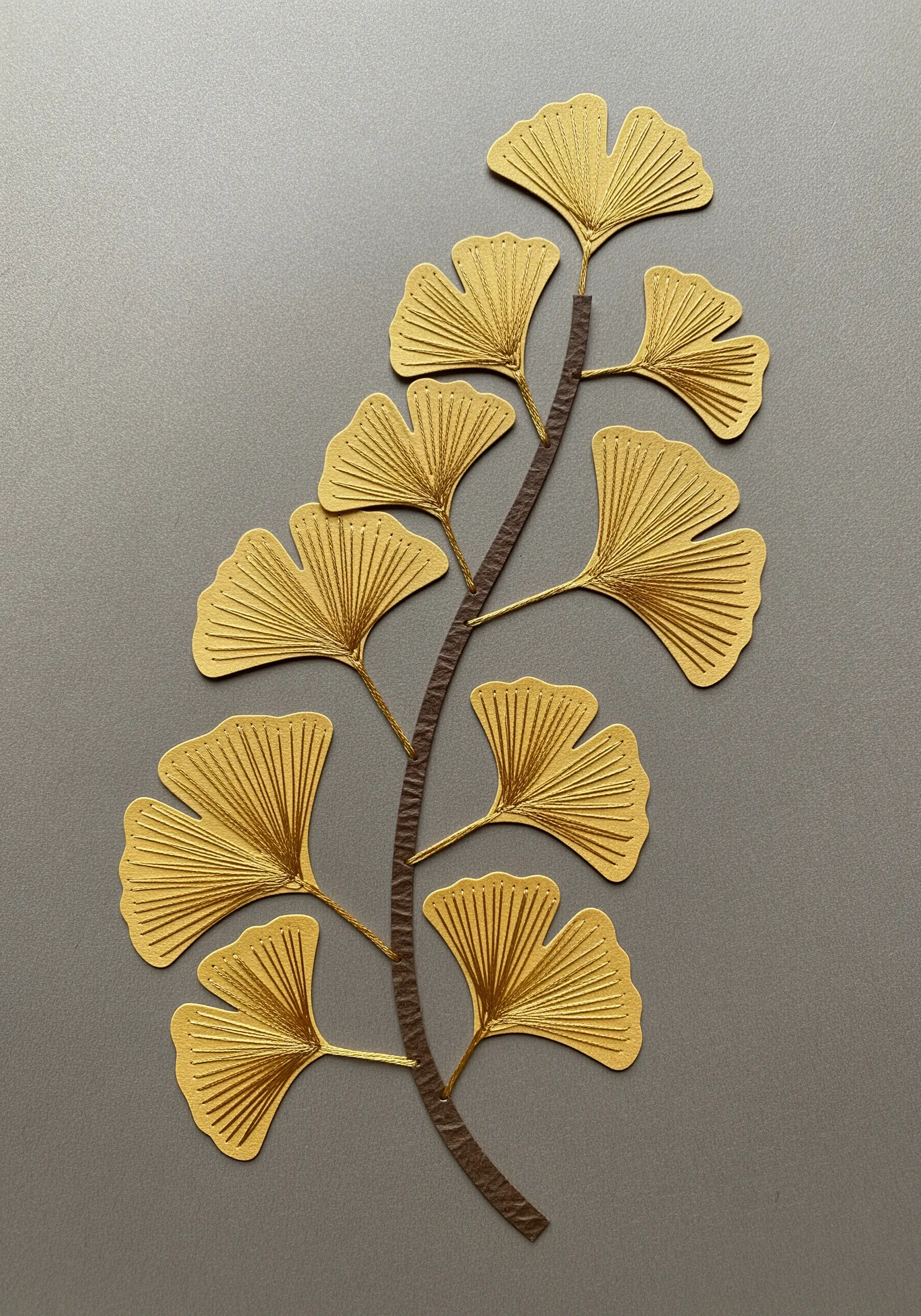 A delicate branch of golden ginkgo leaves made from paper, with fine lines suggesting veins.