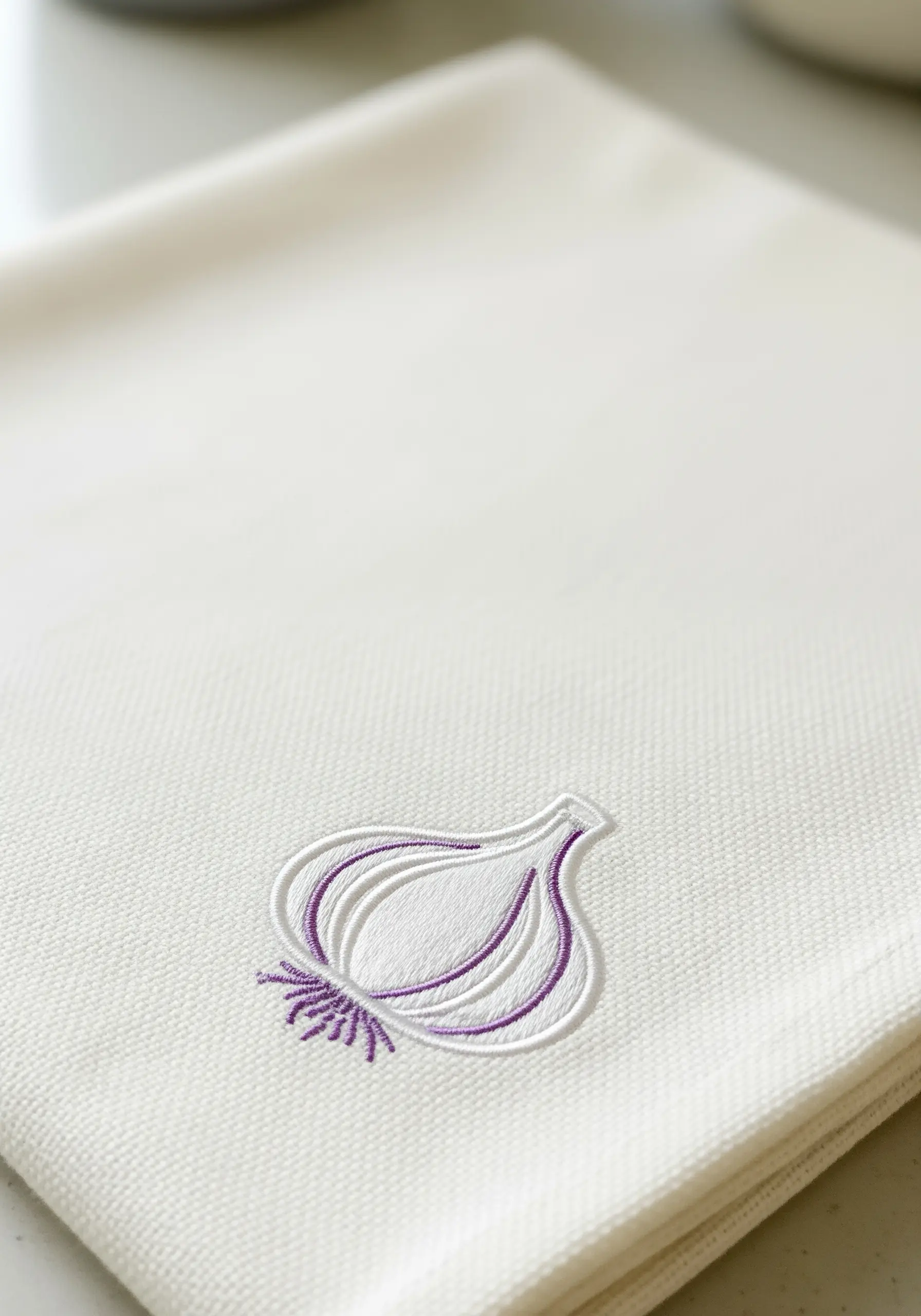 A minimalist line art embroidery of a garlic bulb with purple details on a white towel.