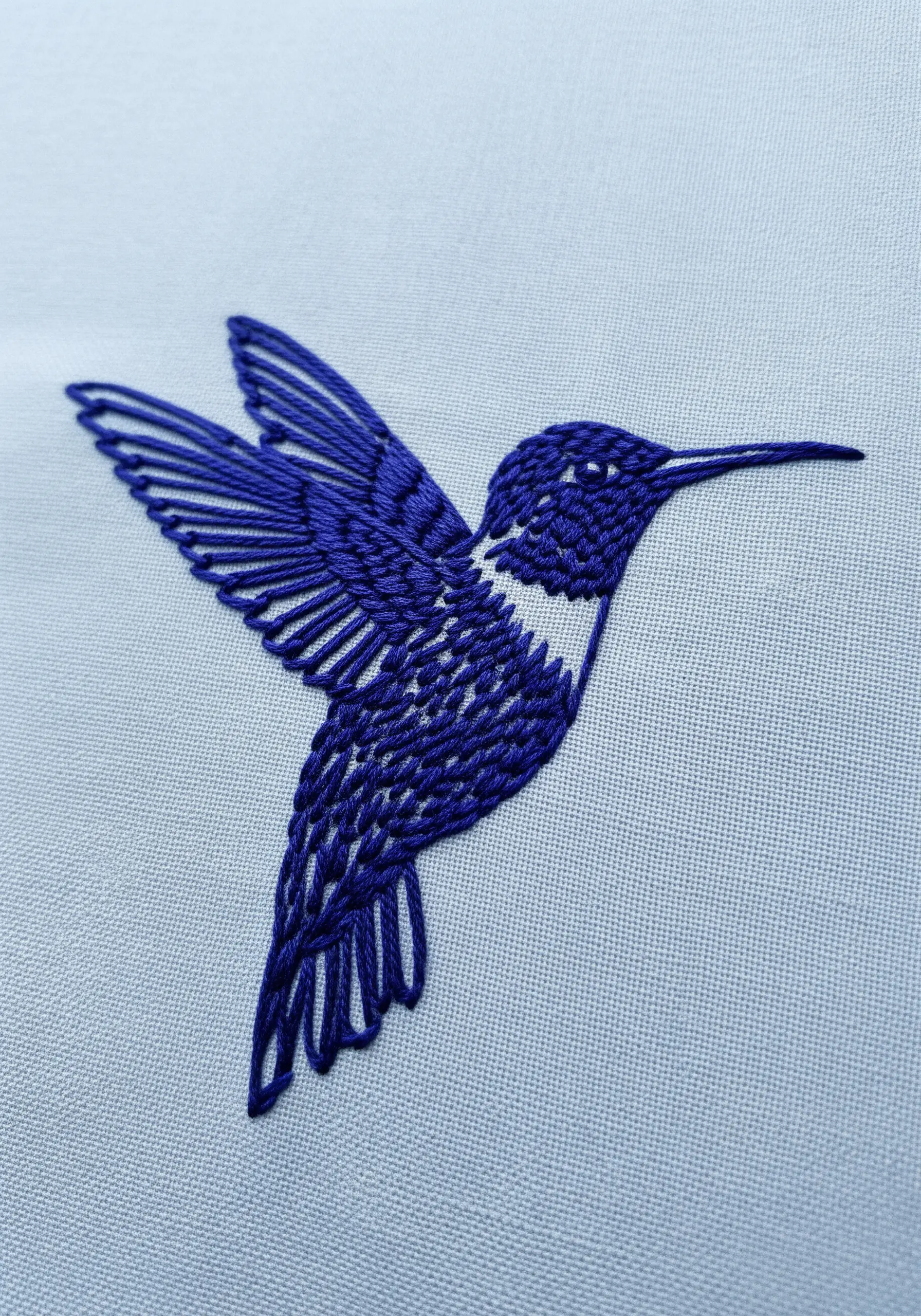 A hummingbird embroidered in blue, using open fill stitches to create texture.