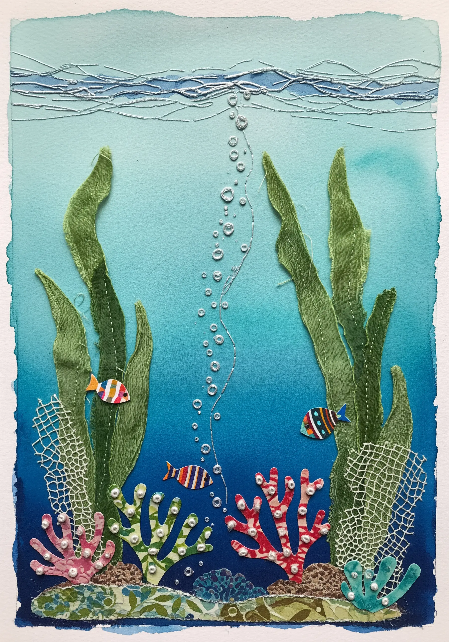Underwater collage with fabric seaweed, paper fish, and silver thread bubbles.