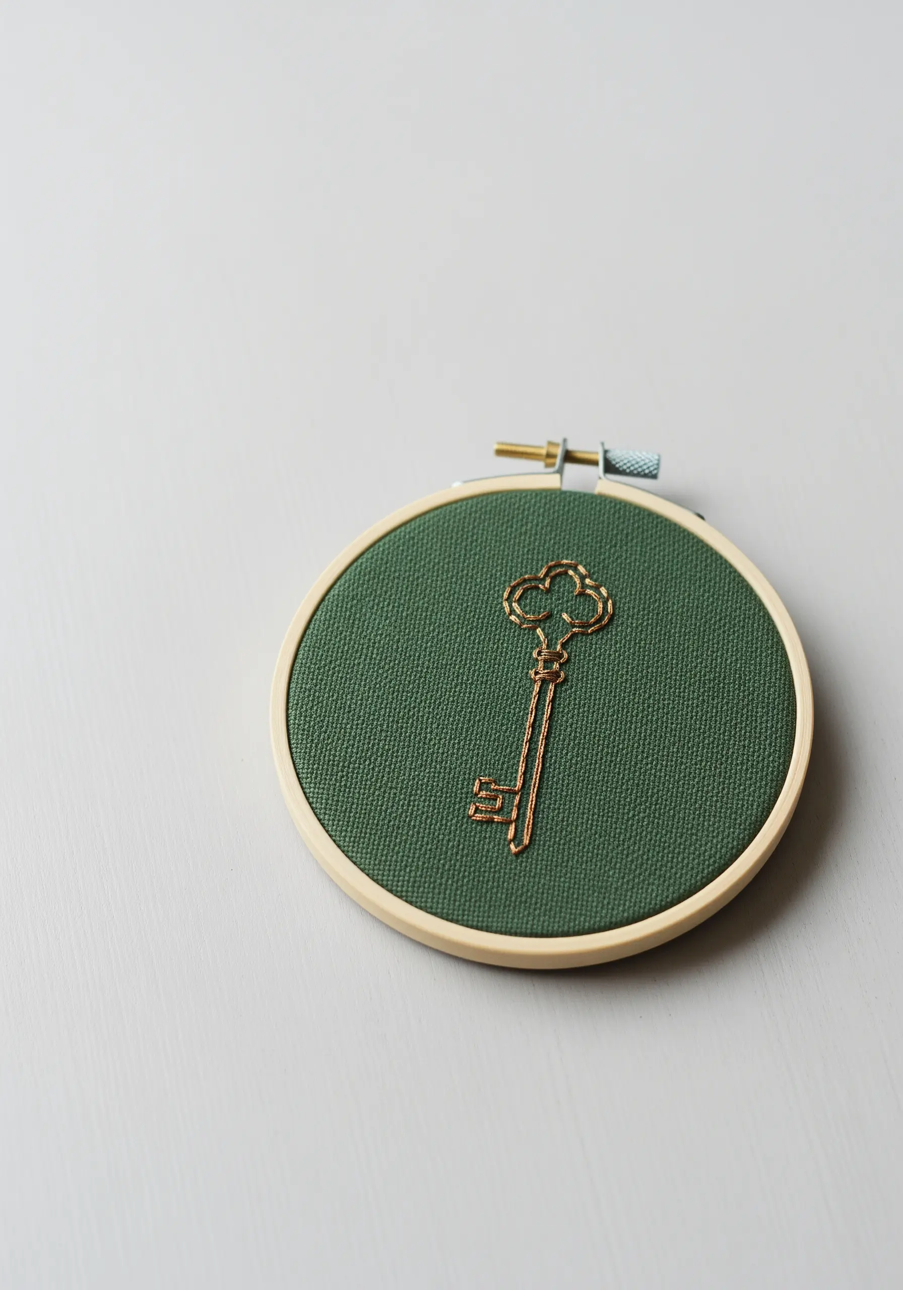 An antique-style key embroidered in shiny gold metallic thread on dark green fabric.
