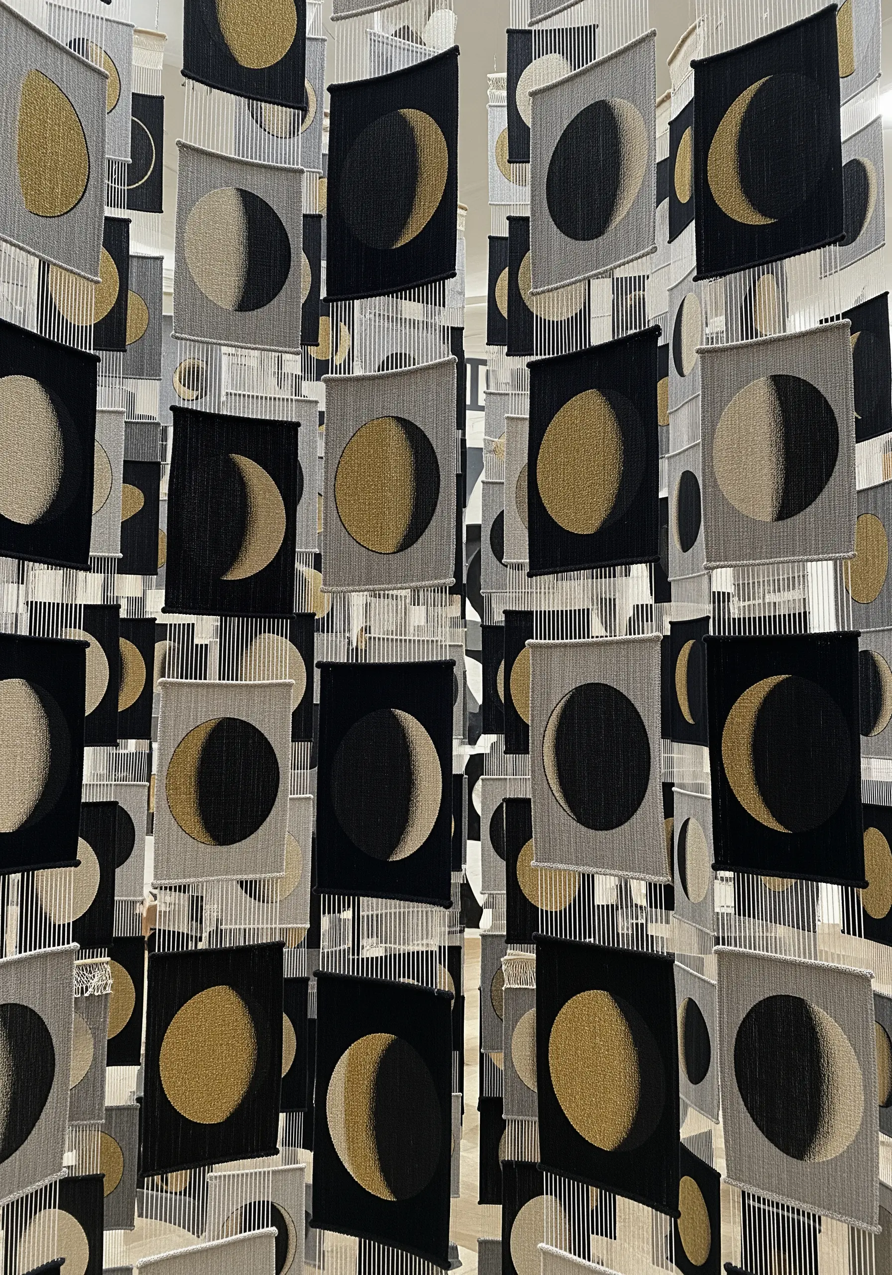 An installation of many small, woven panels depicting phases of the moon.
