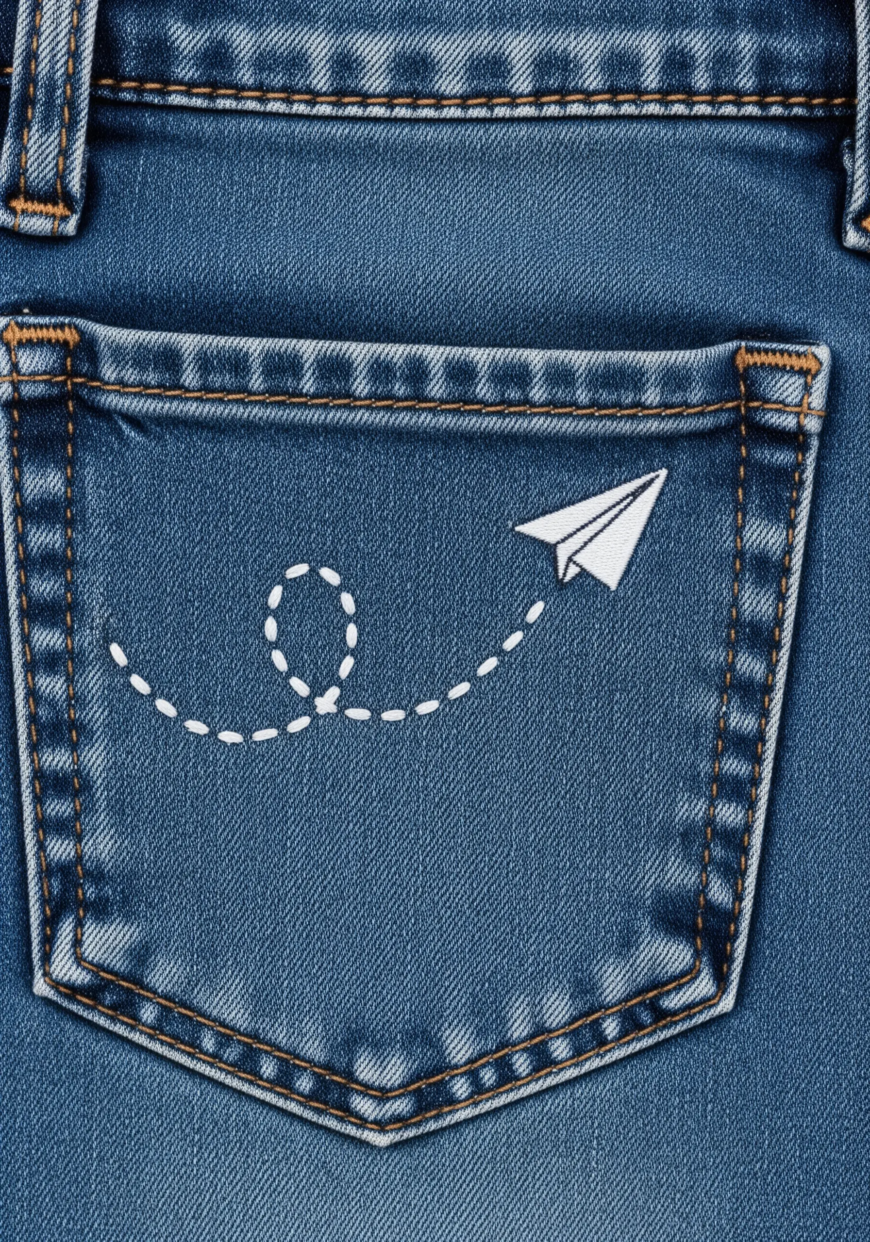 A paper airplane embroidered on a denim pocket with a dashed-line trail behind it.