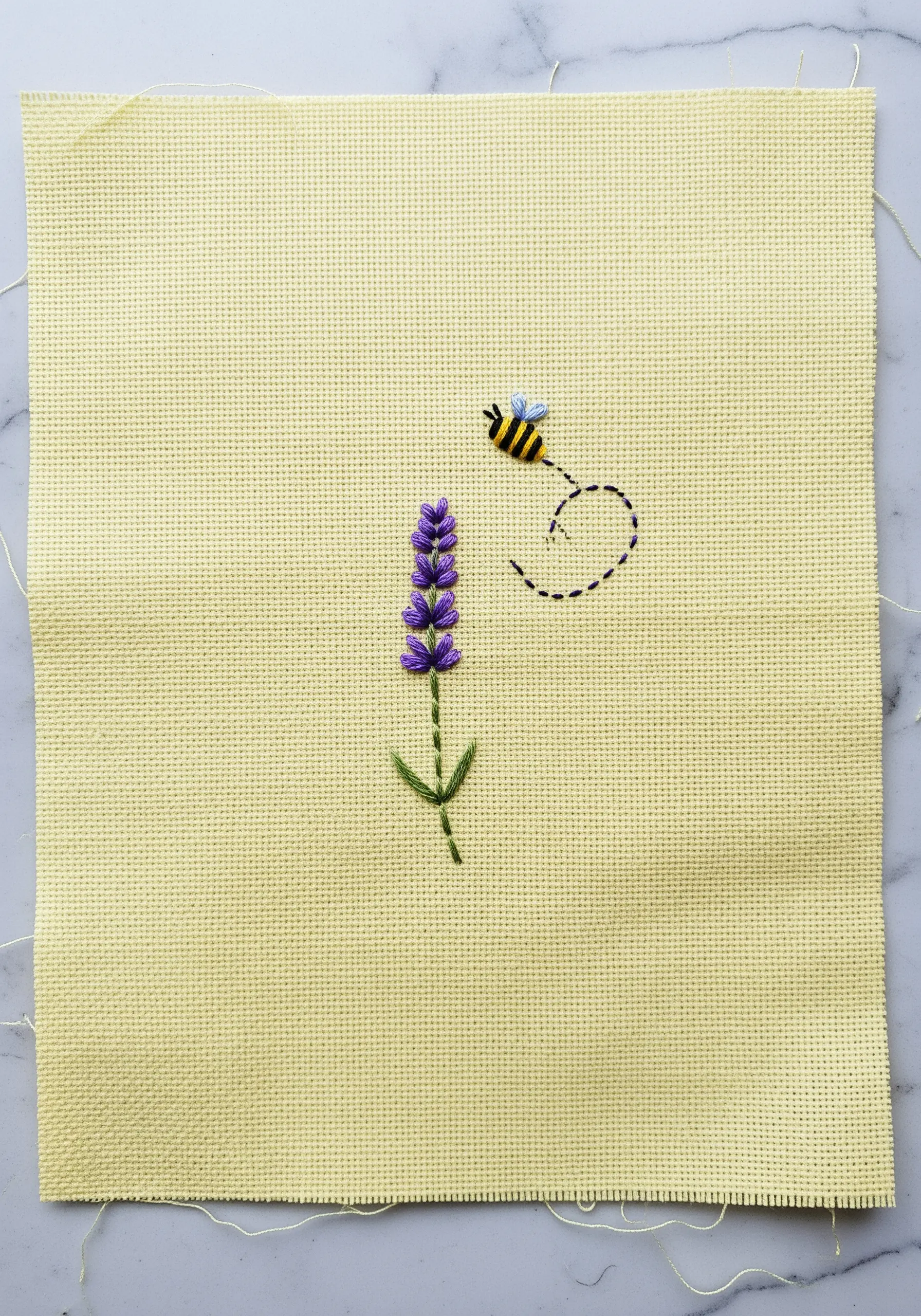 A small embroidered lavender stalk with a bumblebee and a stitched flight path.