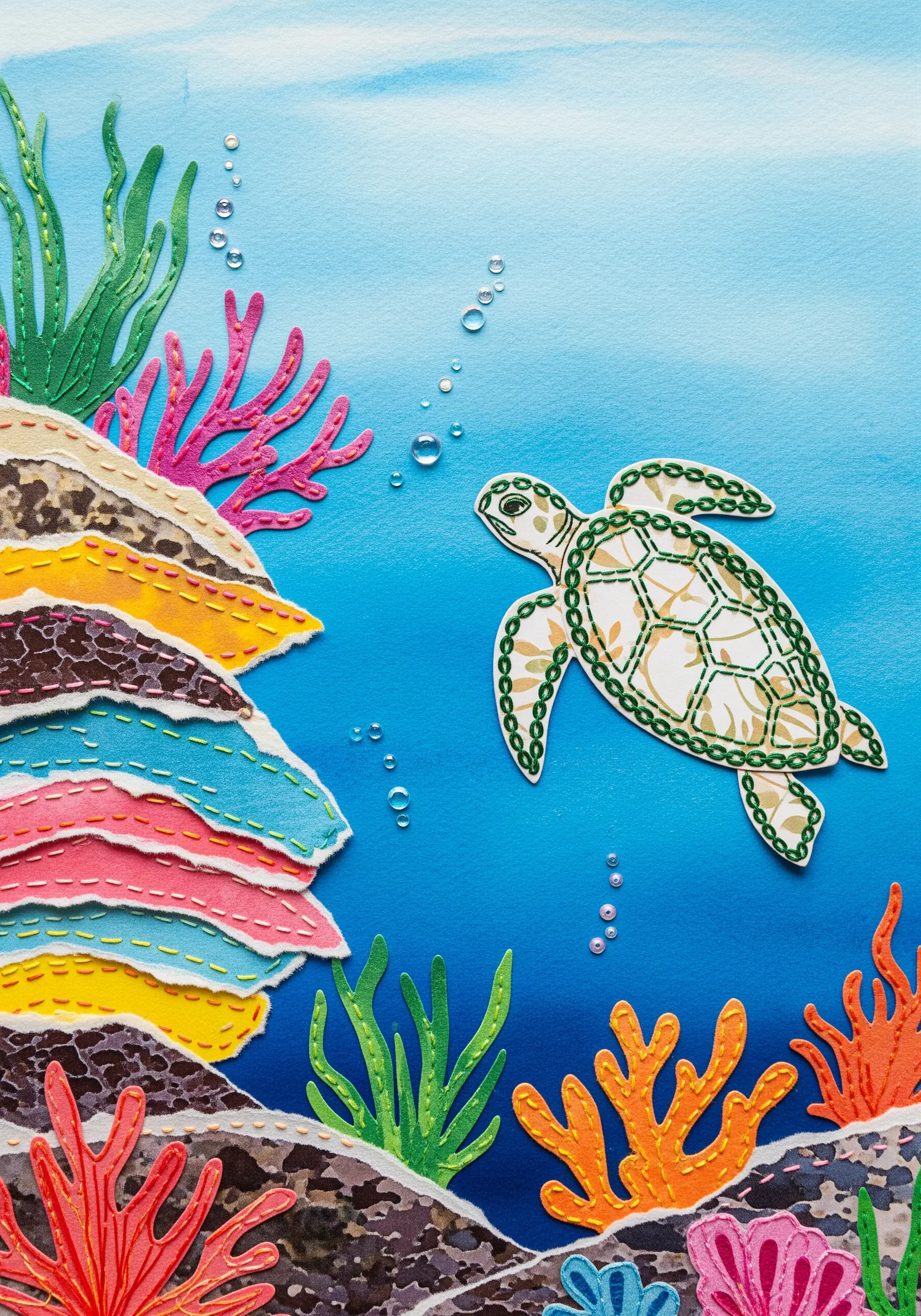 An underwater scene collage with a sea turtle, layered paper coral, and stitch details.