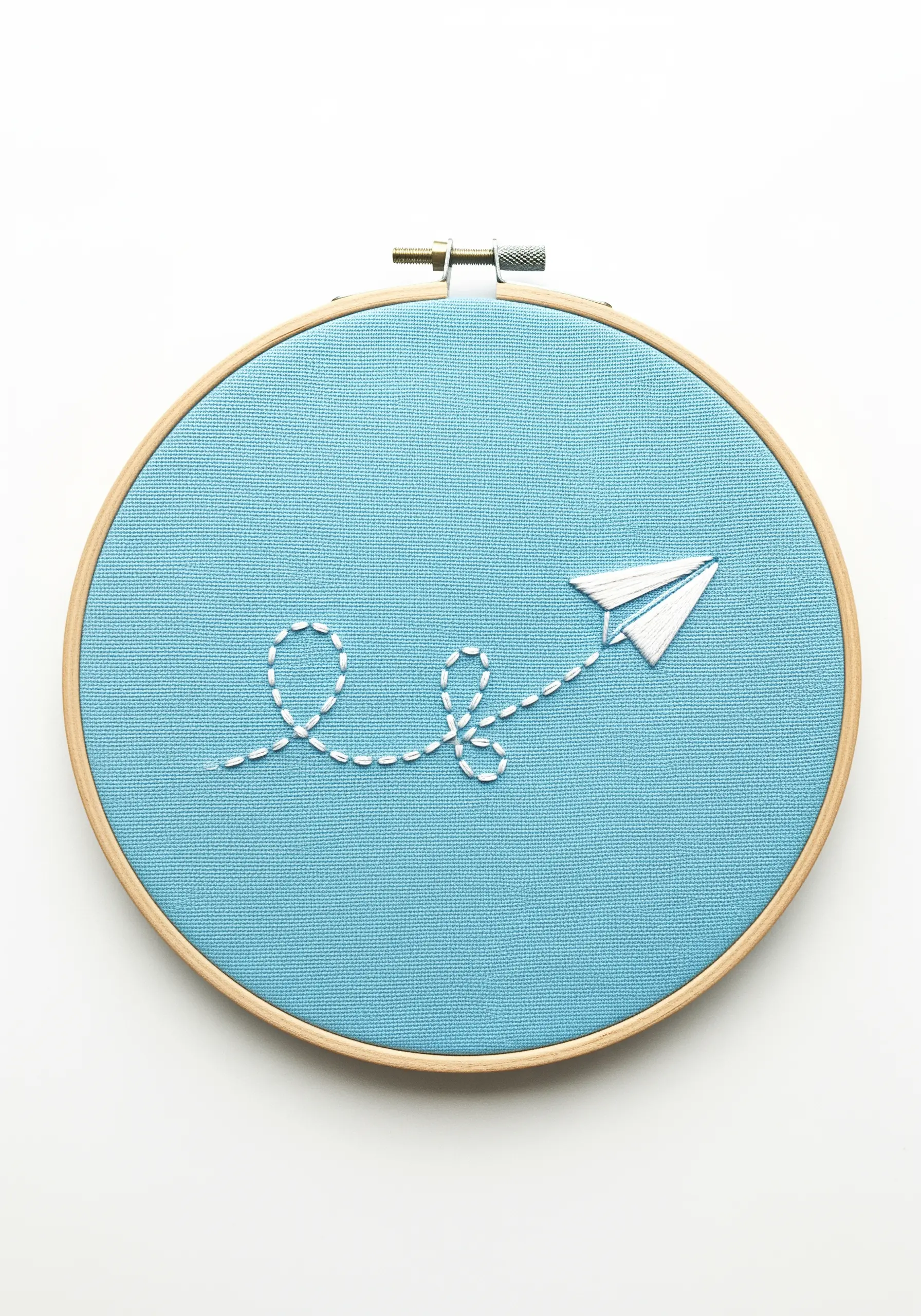 A white paper airplane with a looped, dashed-line trail embroidered on bright blue fabric.