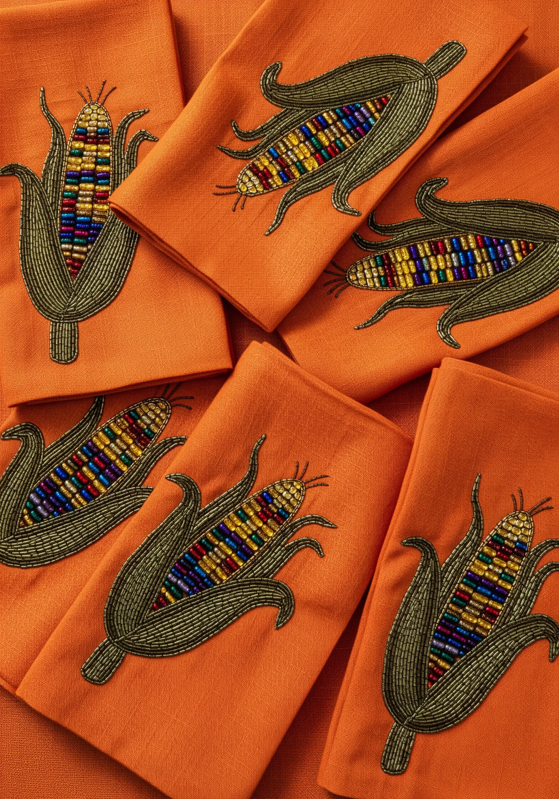 Embroidered Indian corn cobs with multi-colored seed bead kernels on orange napkins.