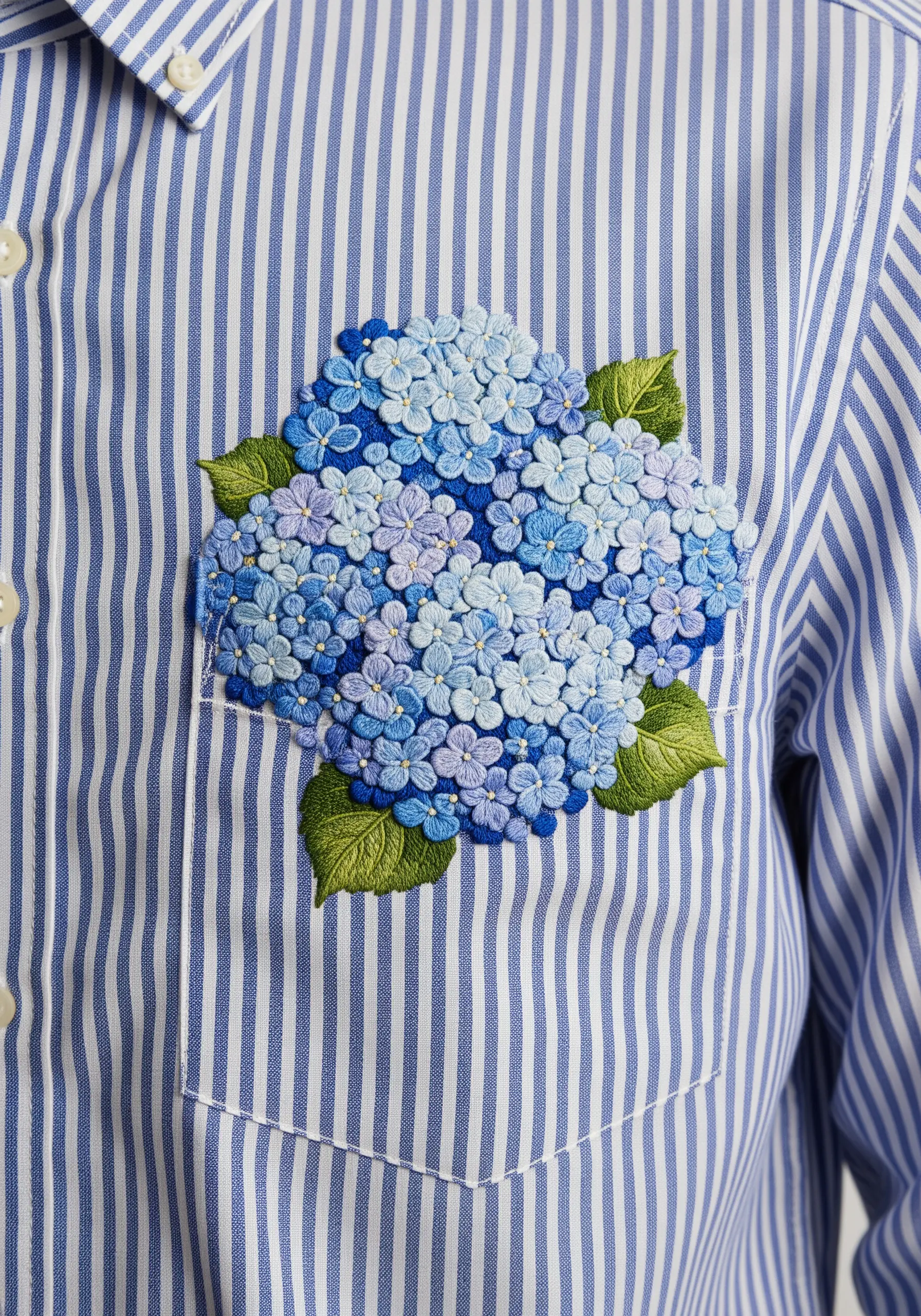 A dense cluster of blue and purple hydrangeas made of French knots on a striped shirt.