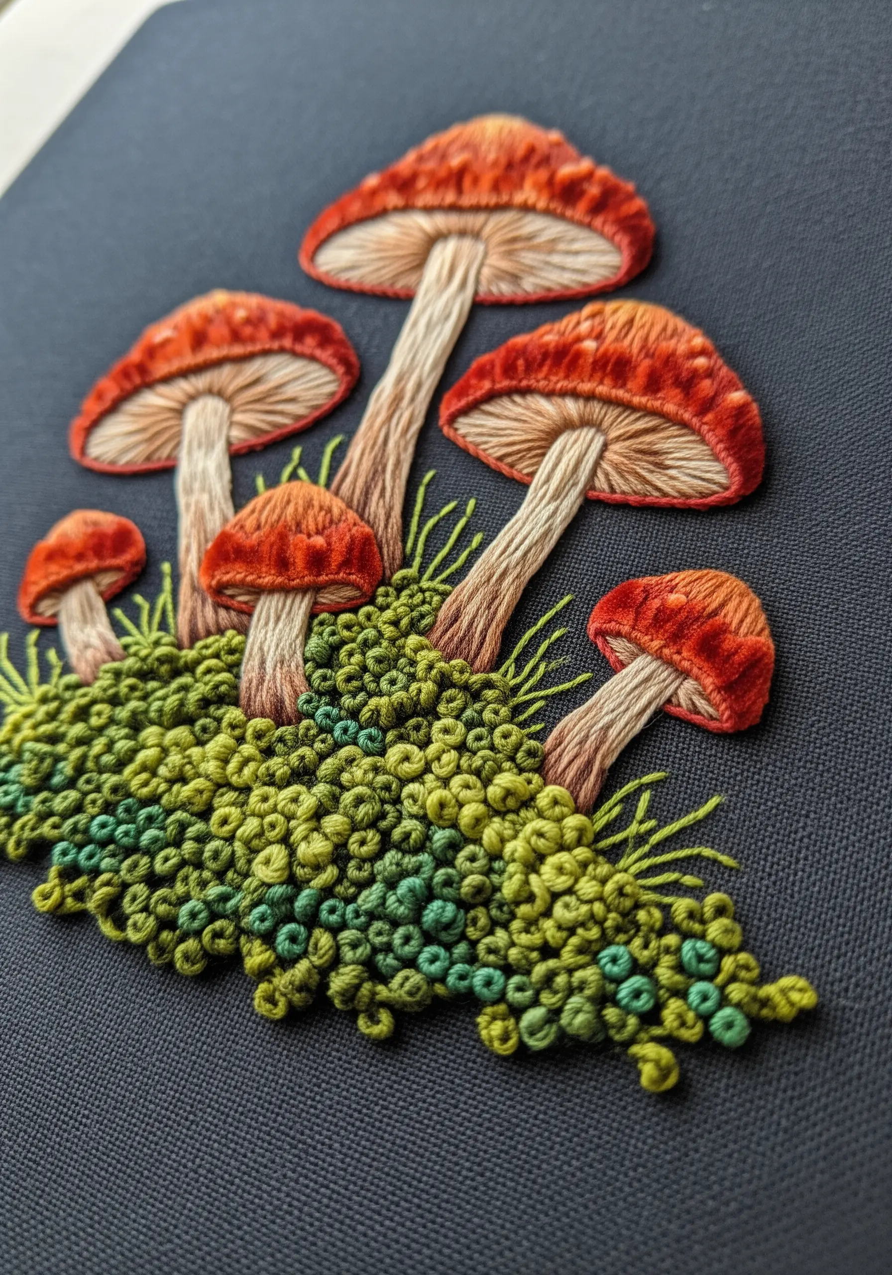 Embroidery of orange mushrooms on a bed of green French knot moss