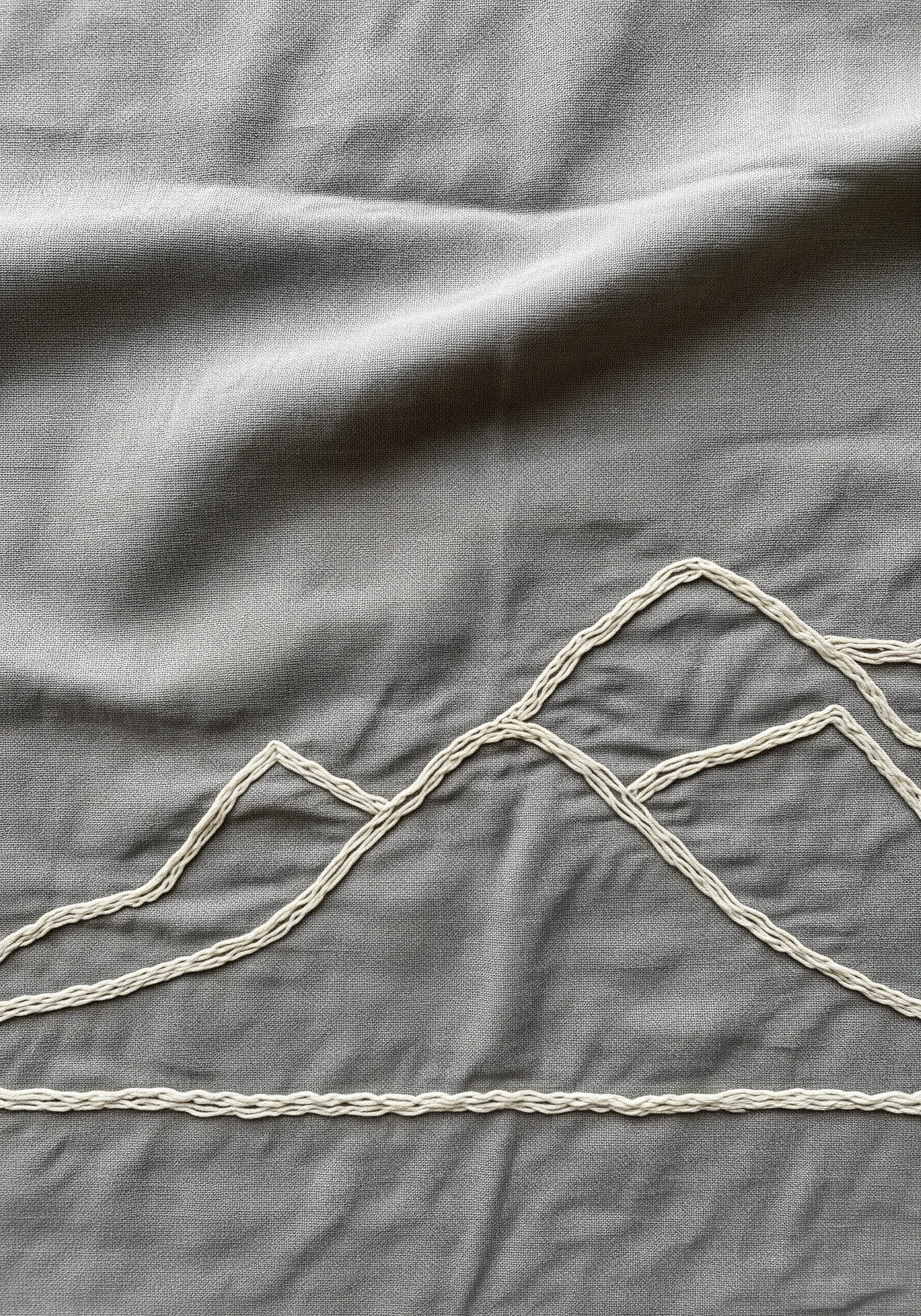 A minimal mountain range embroidered with thick, couched off-white thread on grey fabric.