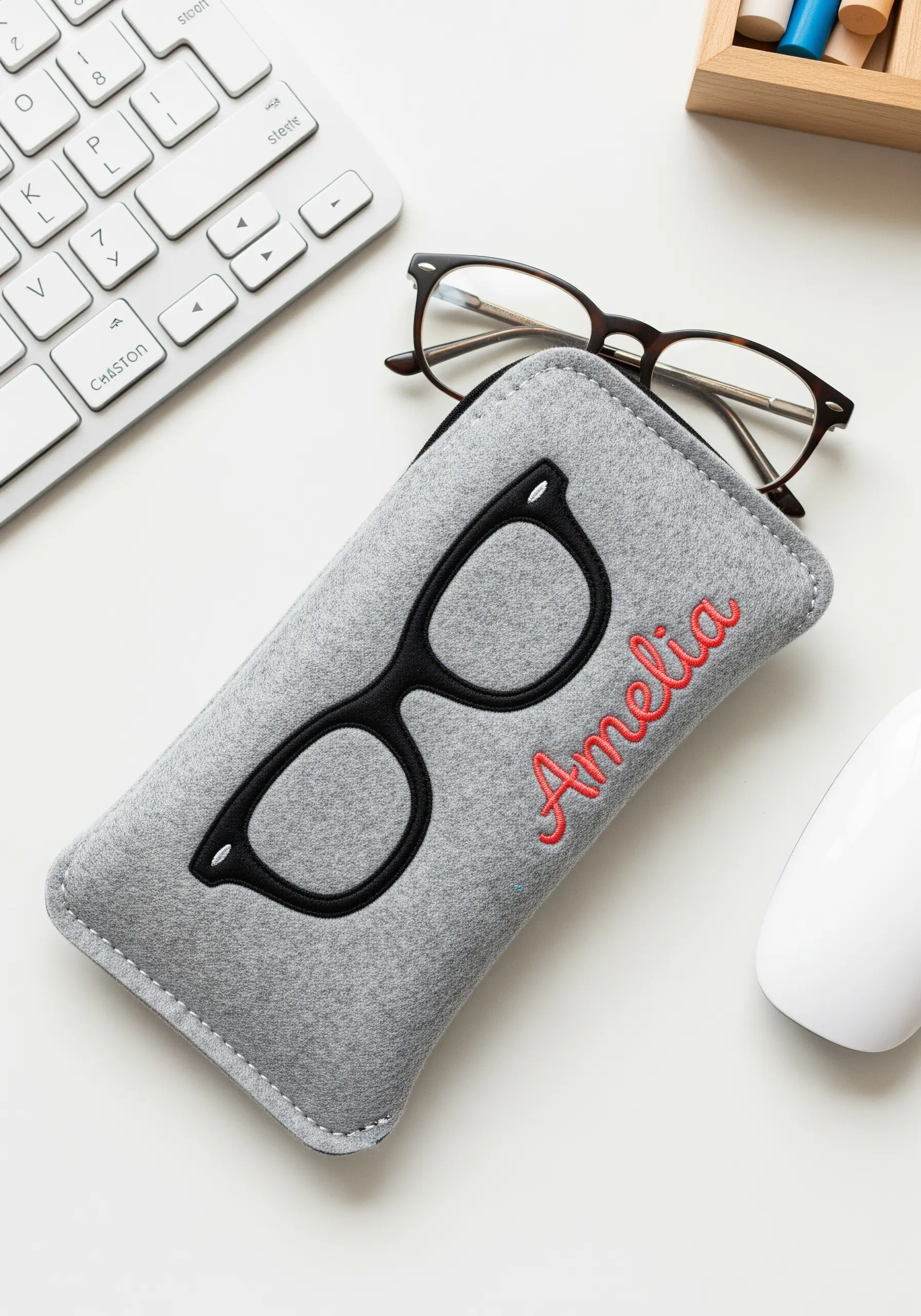A grey felt eyeglass case with a black felt appliqué of cat-eye glasses and a name.