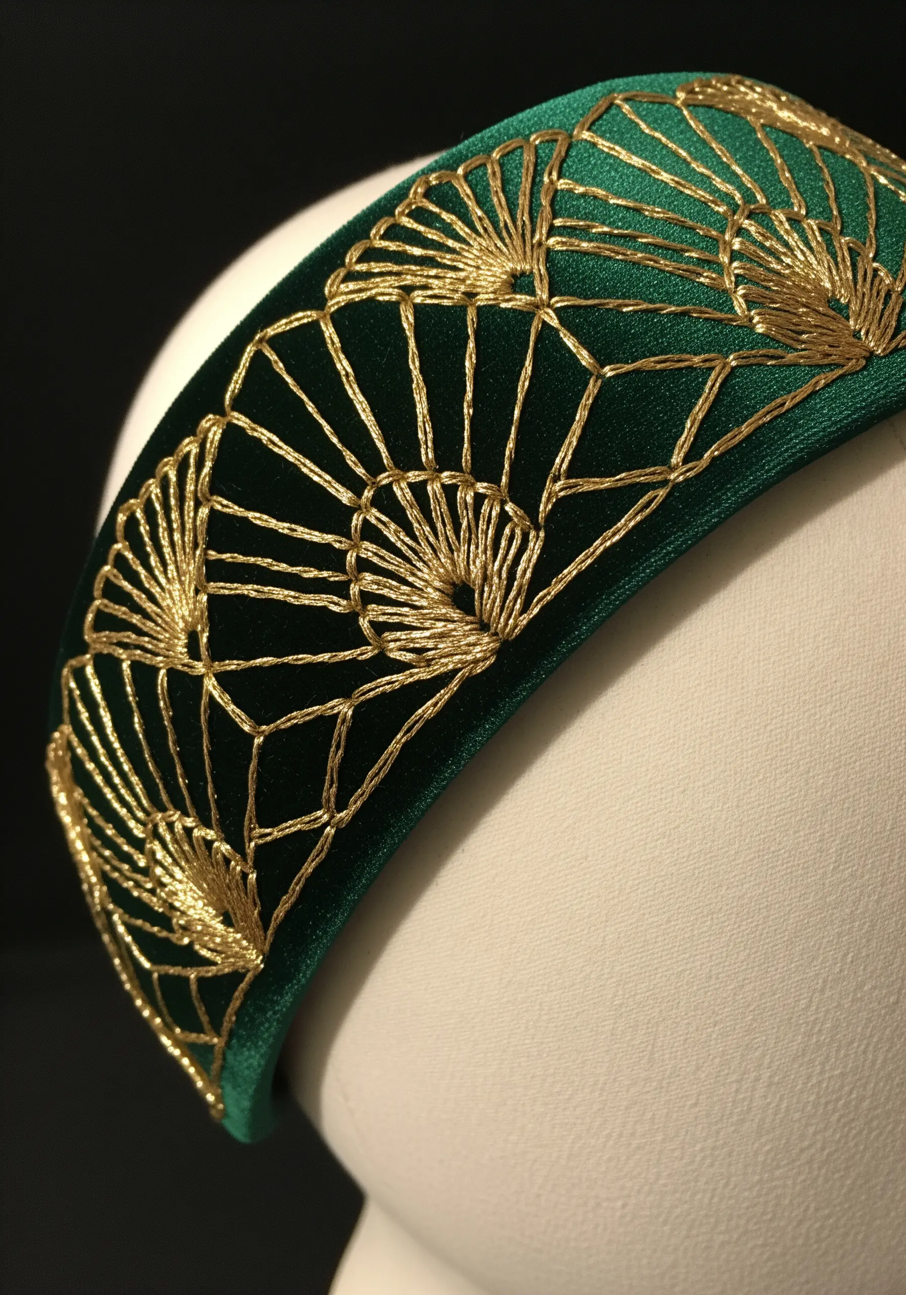 A green velvet headband with a repeating Art Deco fan pattern embroidered in shimmering gold thread.