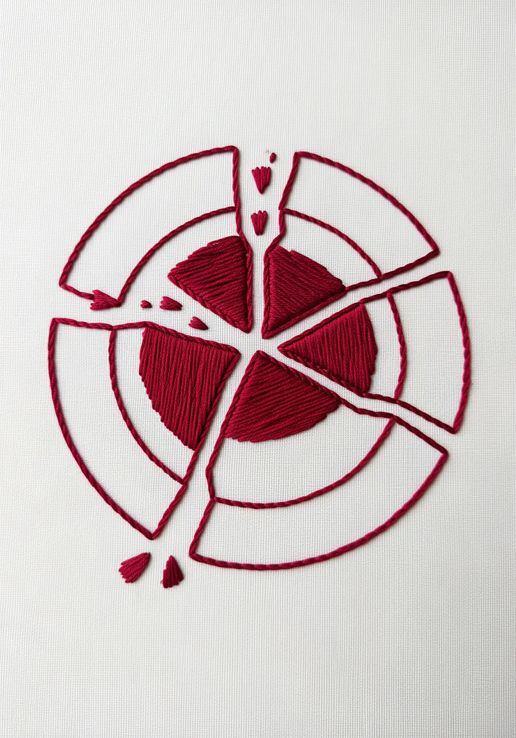 A red embroidered target shape, broken into fragmented pieces on a white background.
