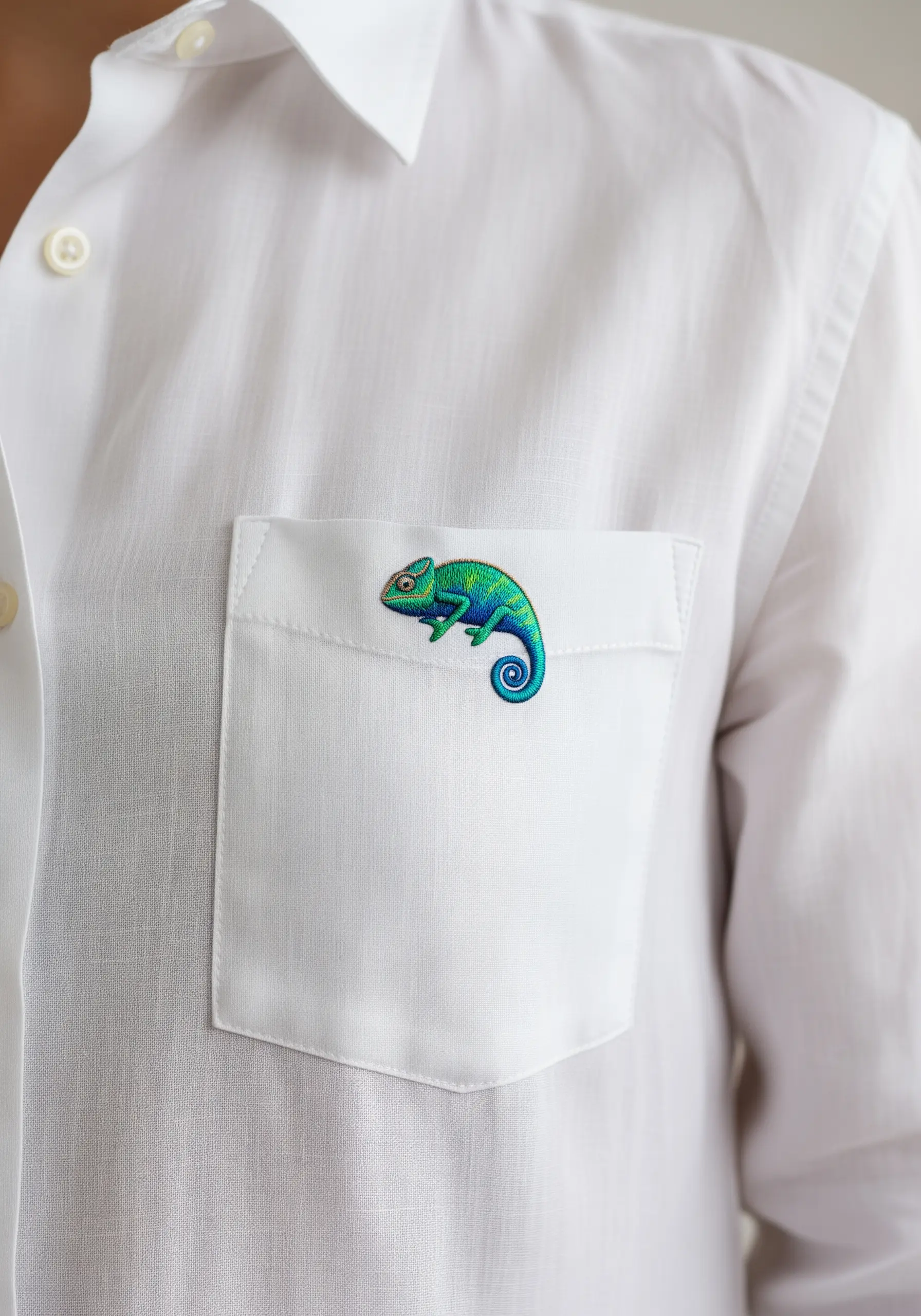 Vibrant thread-painted chameleon with color gradients on a white shirt pocket.