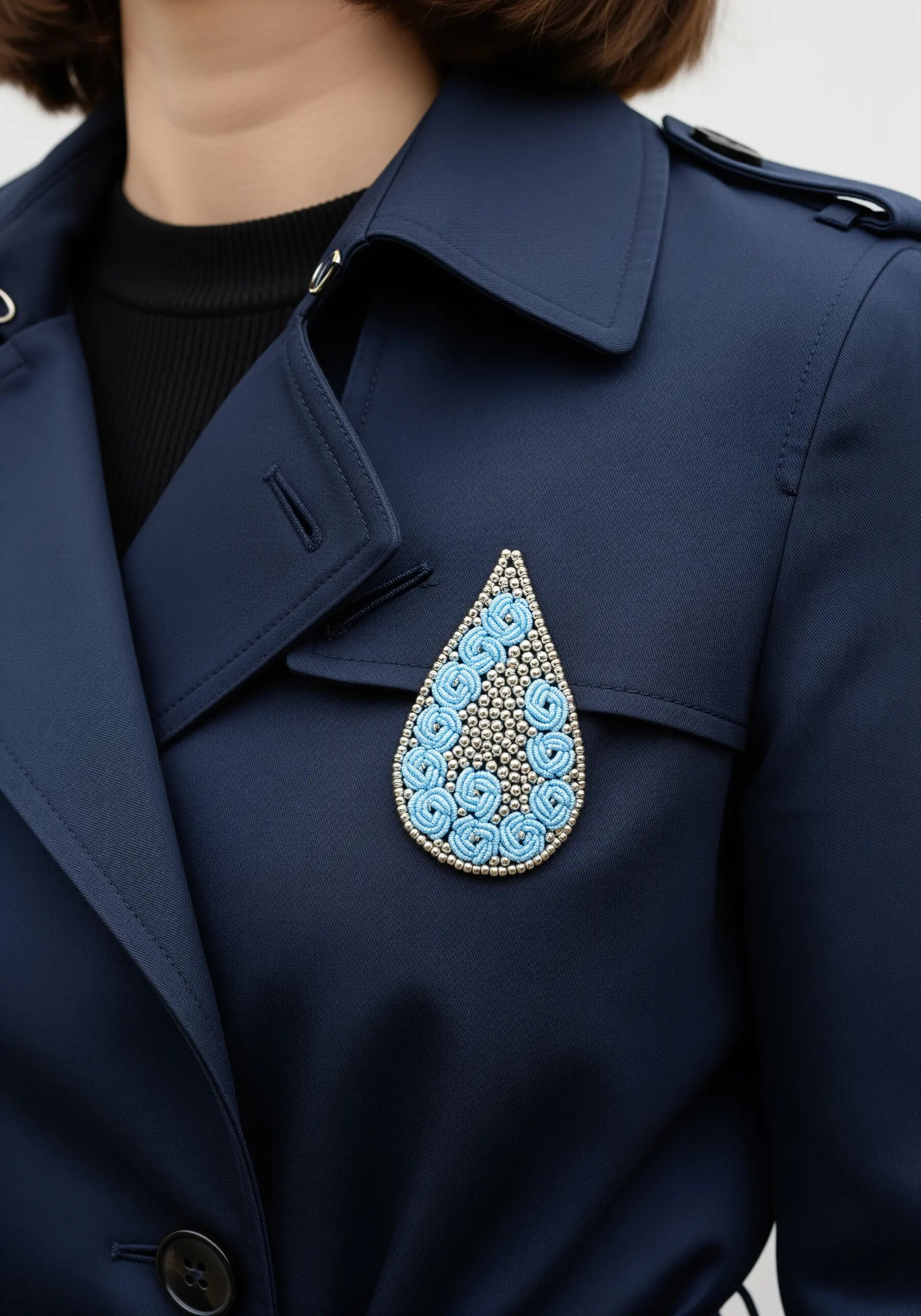A teardrop-shaped brooch with blue thread swirls and silver beads.