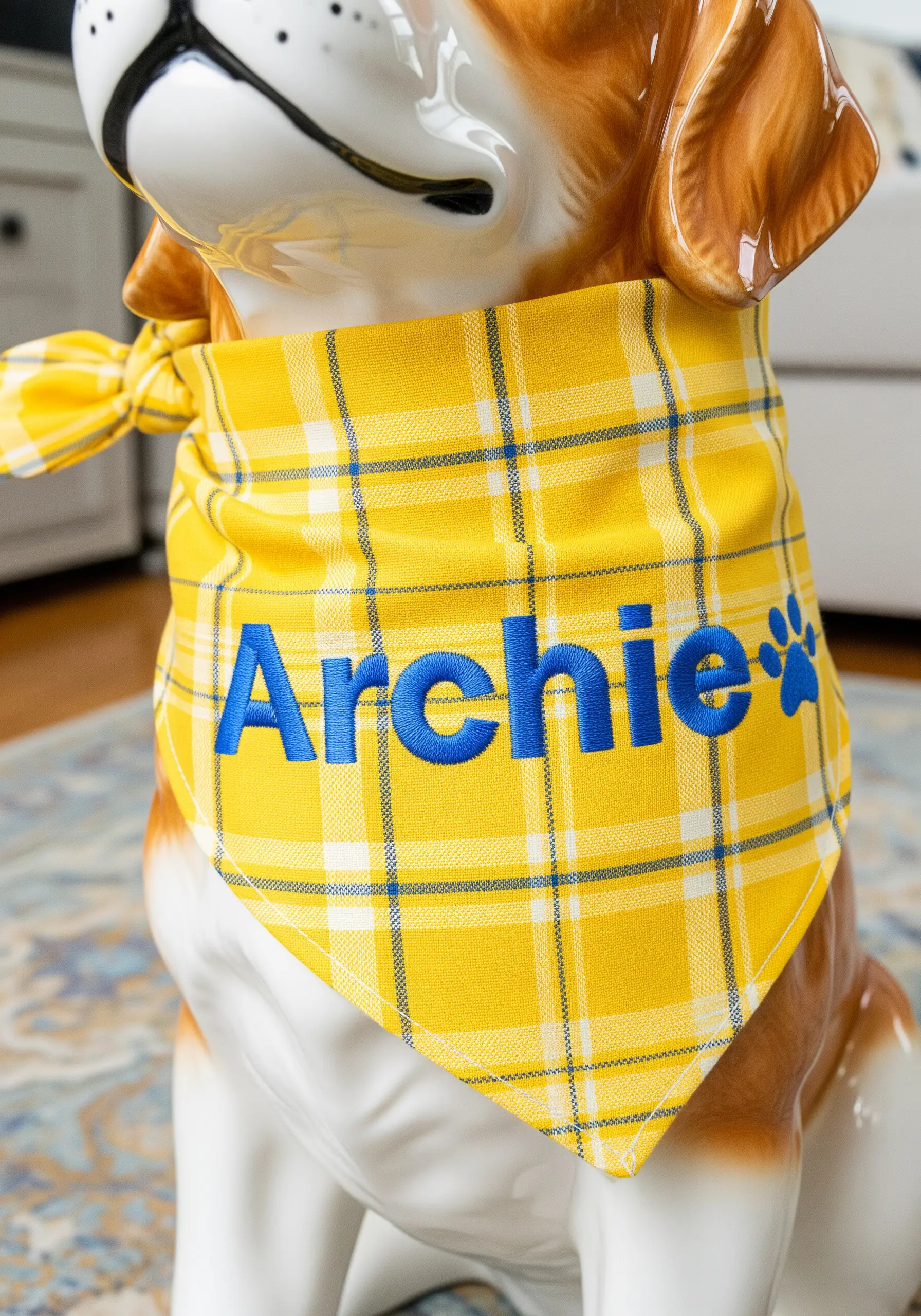 A yellow plaid dog bandana with the name 'Archie' embroidered in bold blue thread.