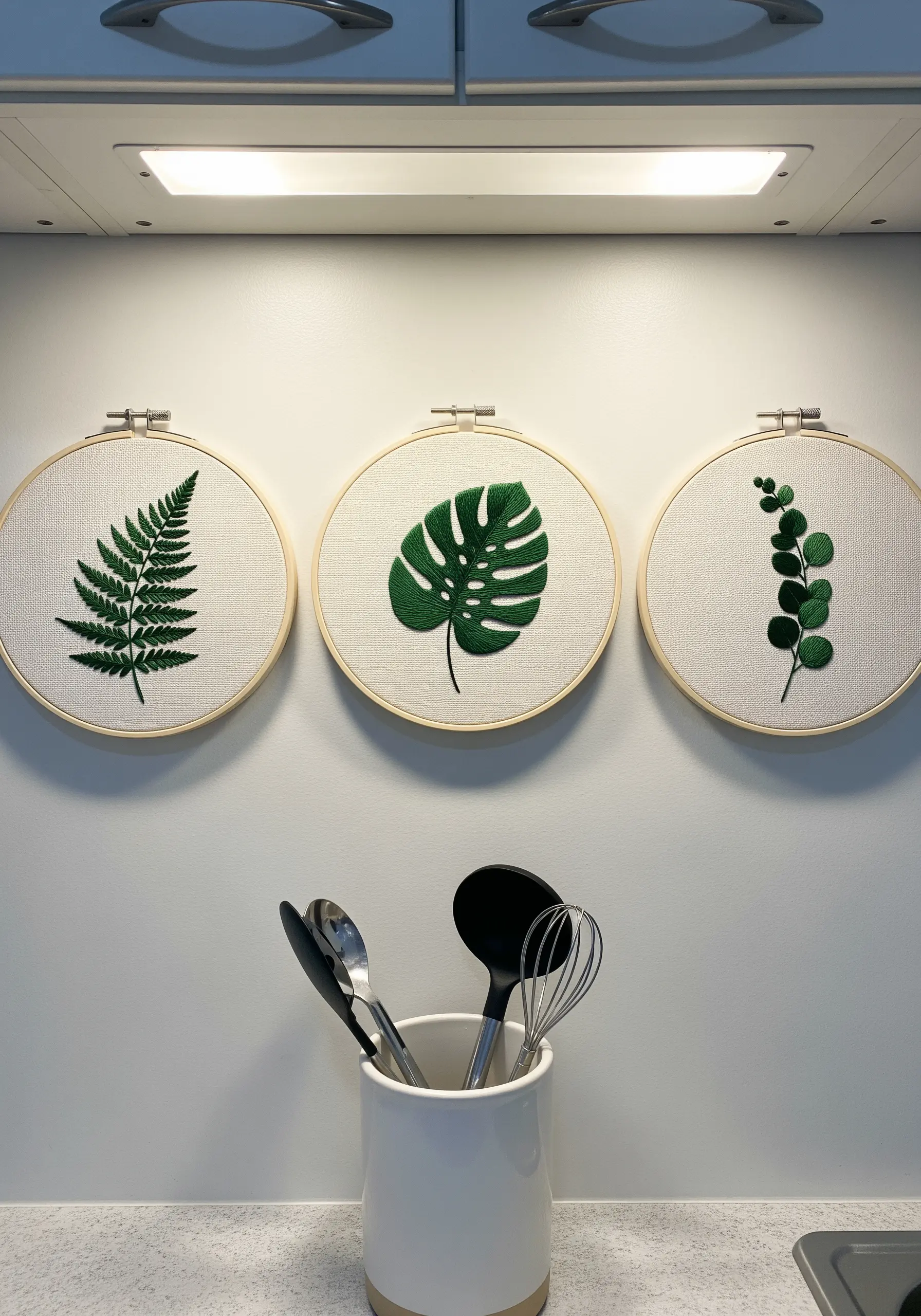 Three embroidery hoops hung in a row, each with a different green leaf design.