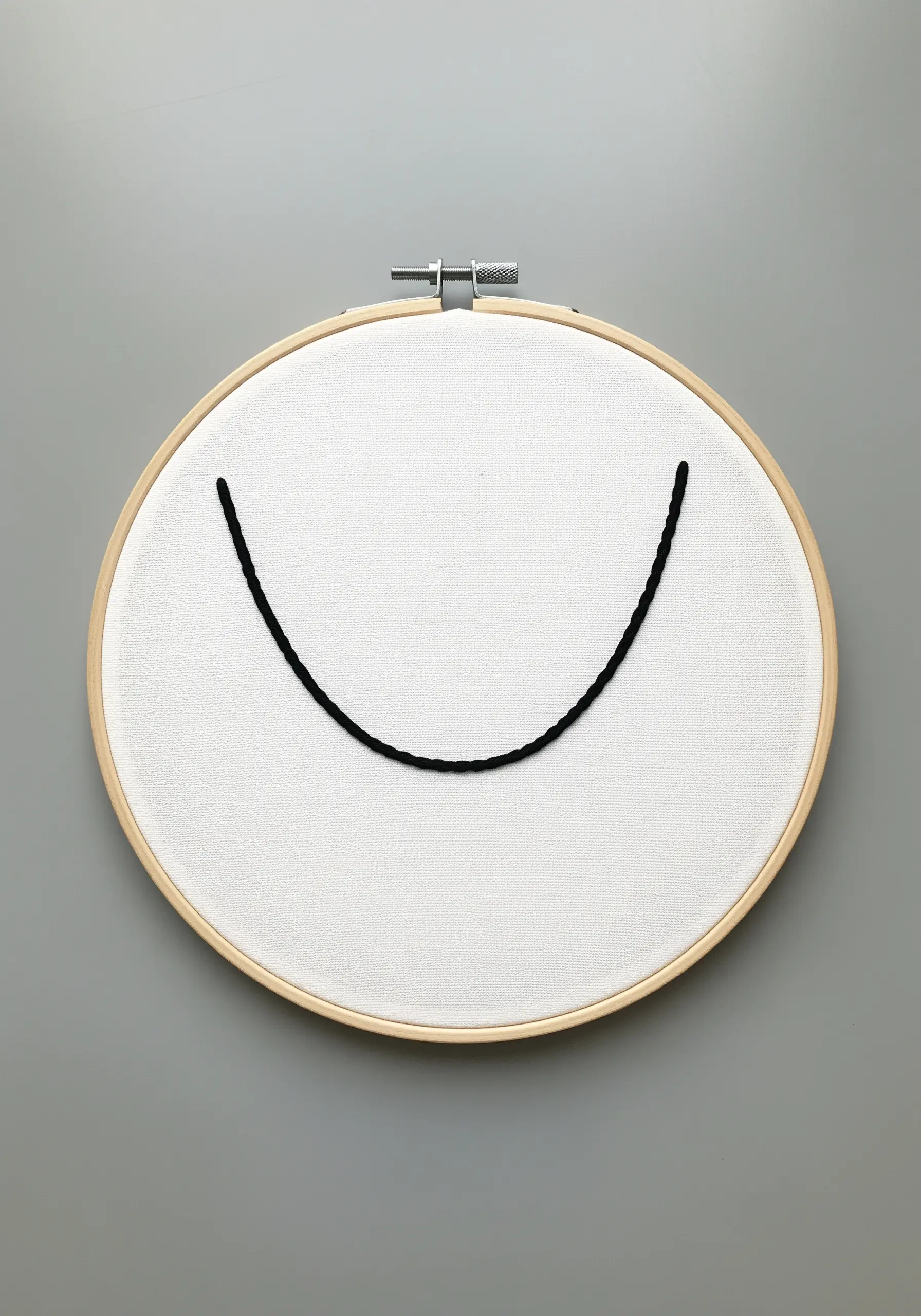 A single, thick black thread hangs in a perfect U-shape curve in an embroidery hoop.