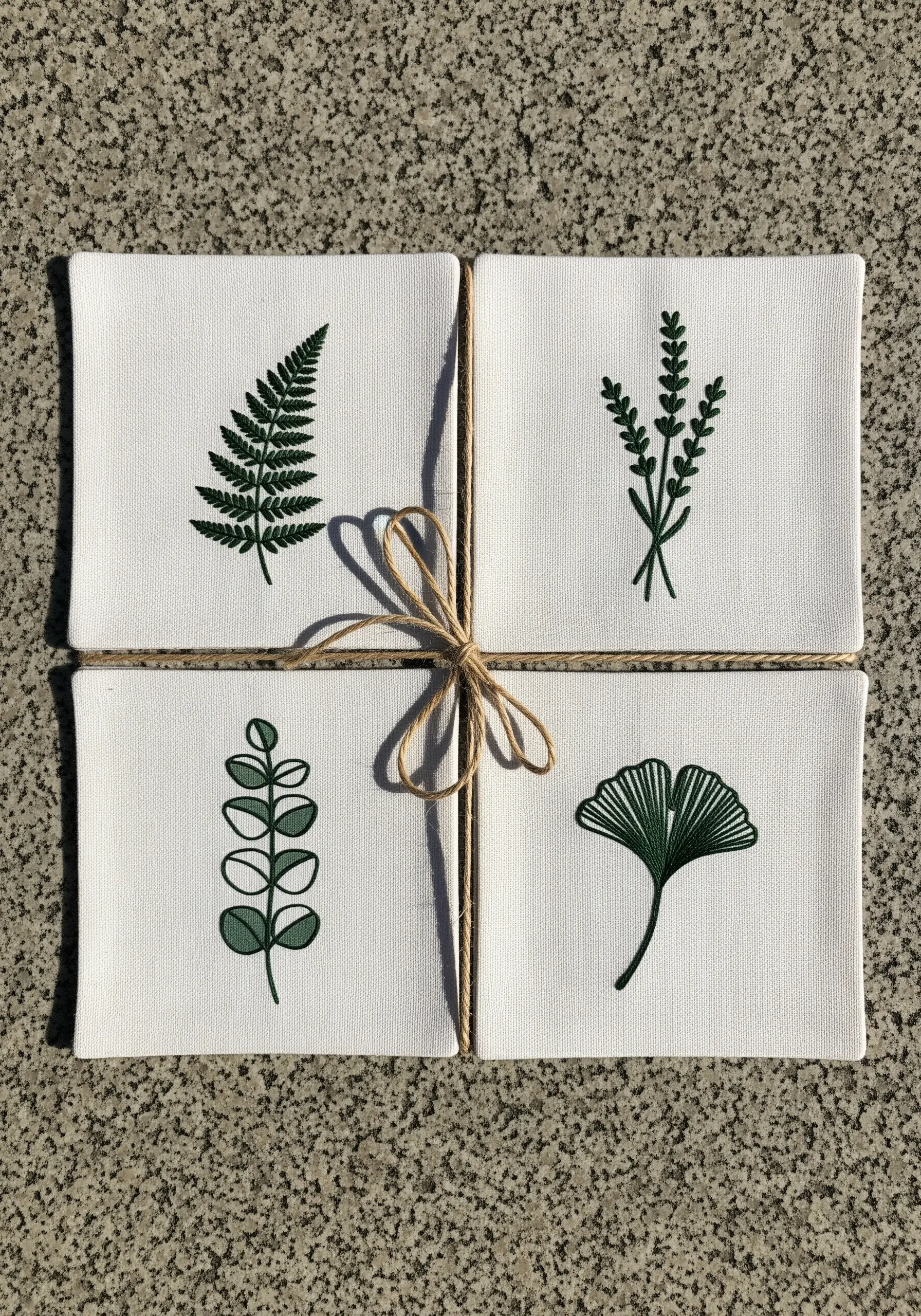 A set of four small canvases, each with a different green botanical embroidery.