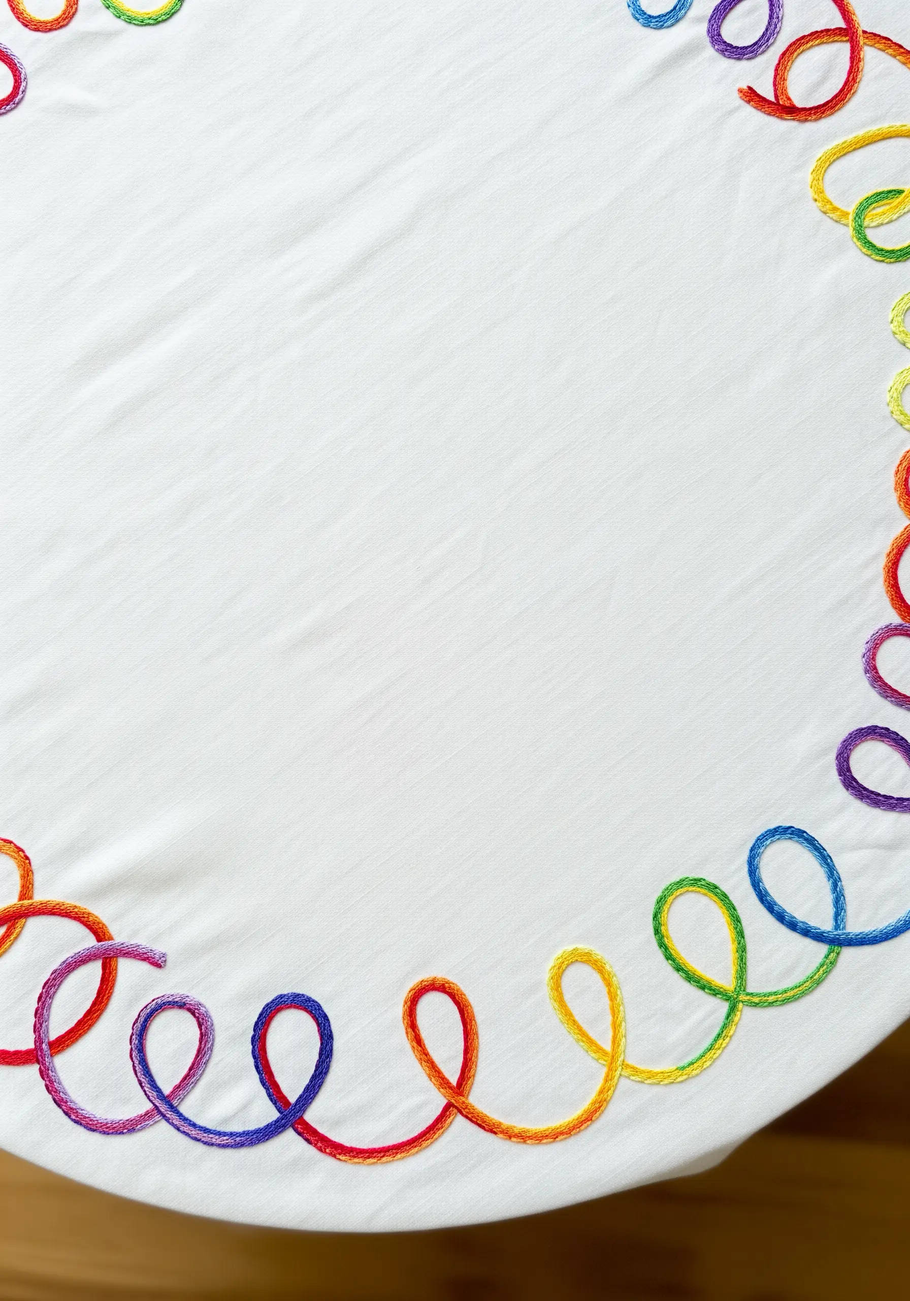 A flowing rainbow ribbon border made with thick satin stitch on a white tablecloth.