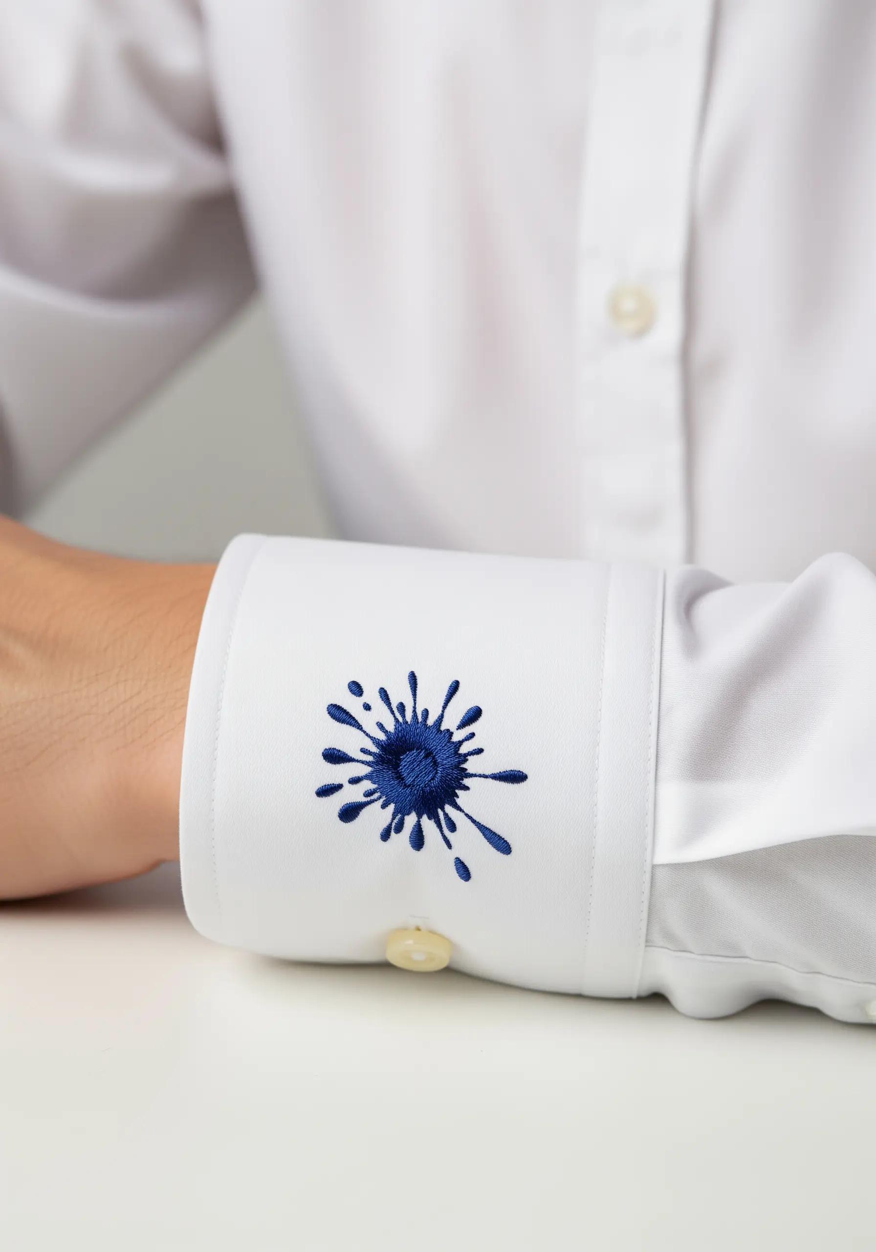 A dark blue embroidered ink splatter on the cuff of a white shirt.