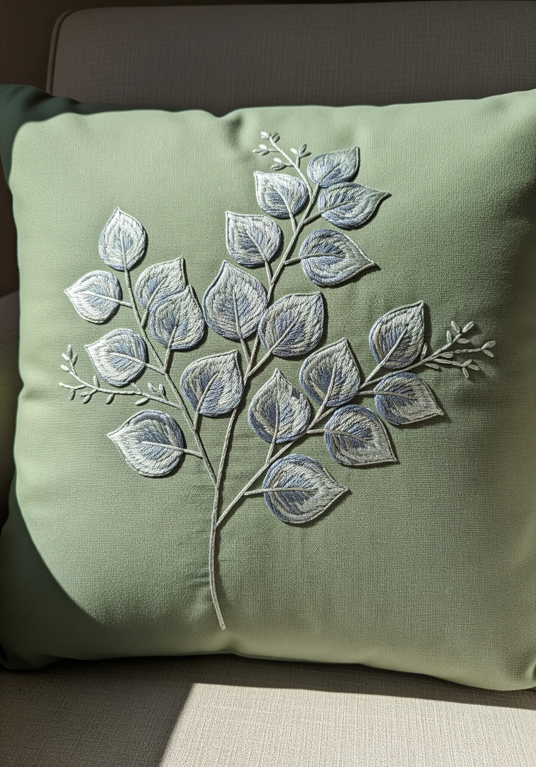 A branch with blue-grey leaves embroidered on a sage green pillow.