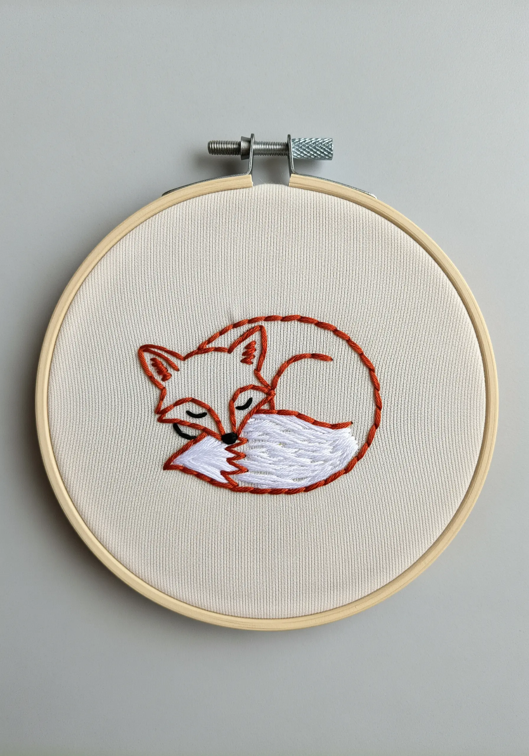 Embroidered sleeping fox with orange outline and white satin stitch tail.
