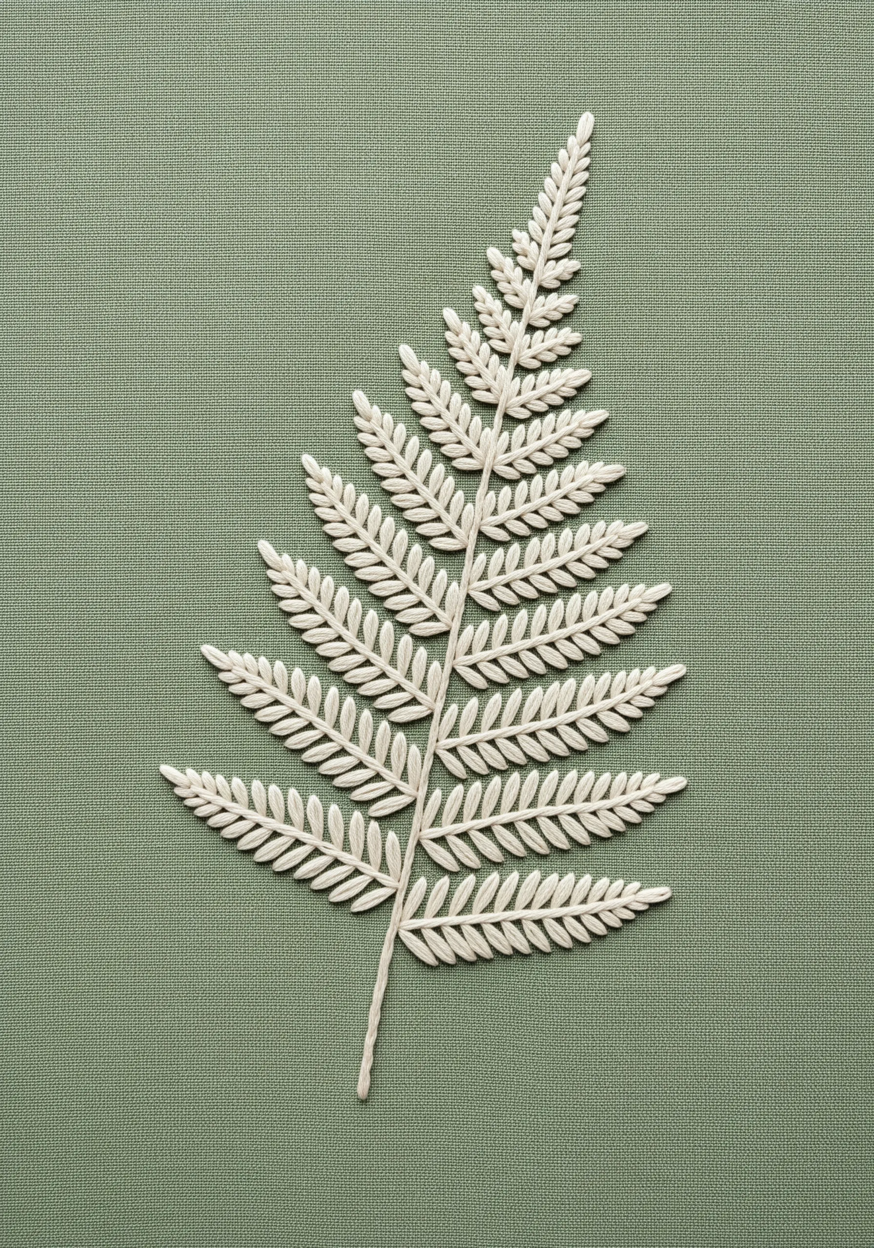 A single fern leaf embroidered in white thread on a sage green fabric.