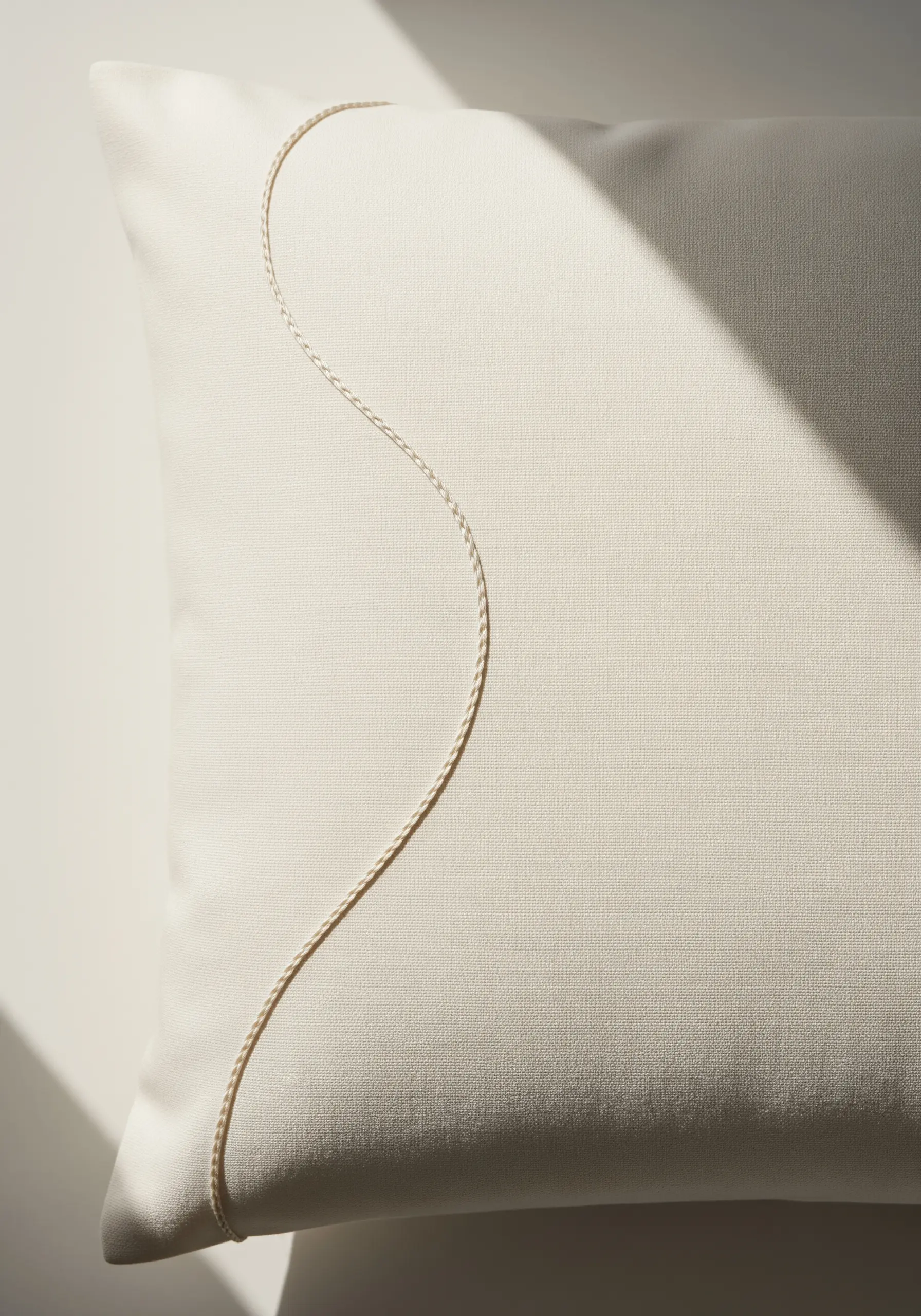 A single, smooth curved line of whipped backstitch on a cream-colored pillow.