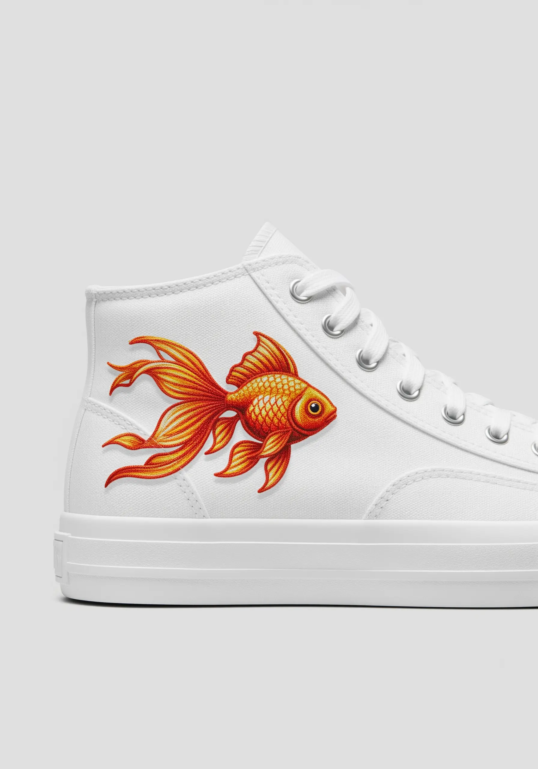 A vibrant, intricately embroidered goldfish with flowing fins on the side of a white canvas sneaker.