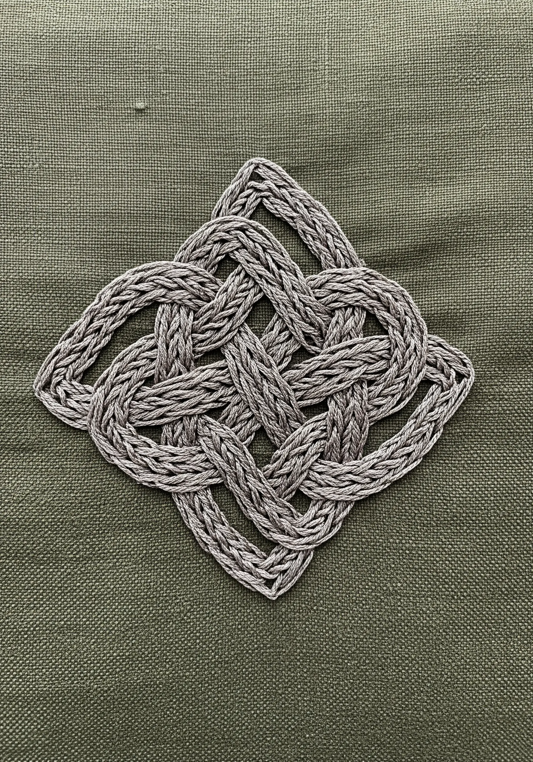 A complex Celtic knot design with a woven texture, embroidered in grey thread on green fabric.