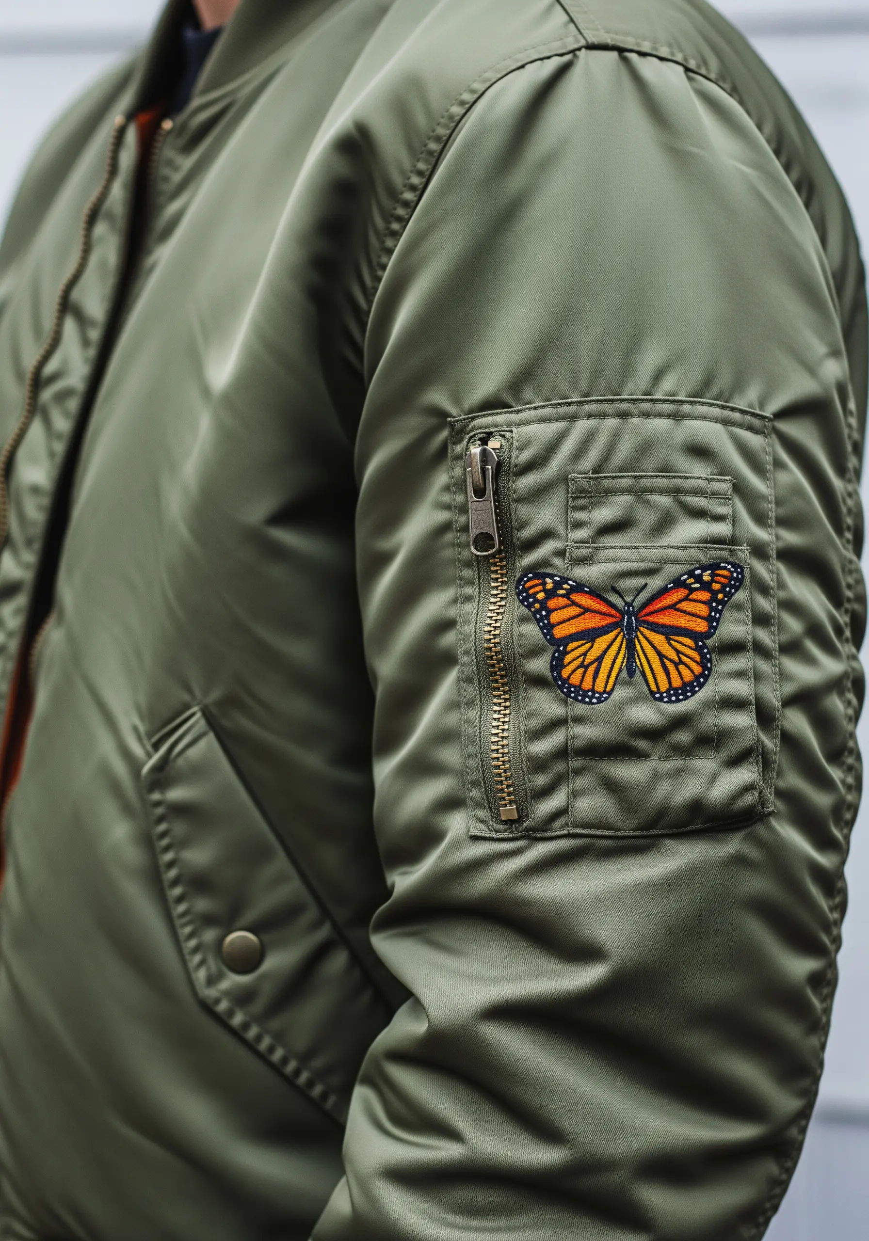 A colorful monarch butterfly patch on the sleeve pocket of an olive bomber jacket.