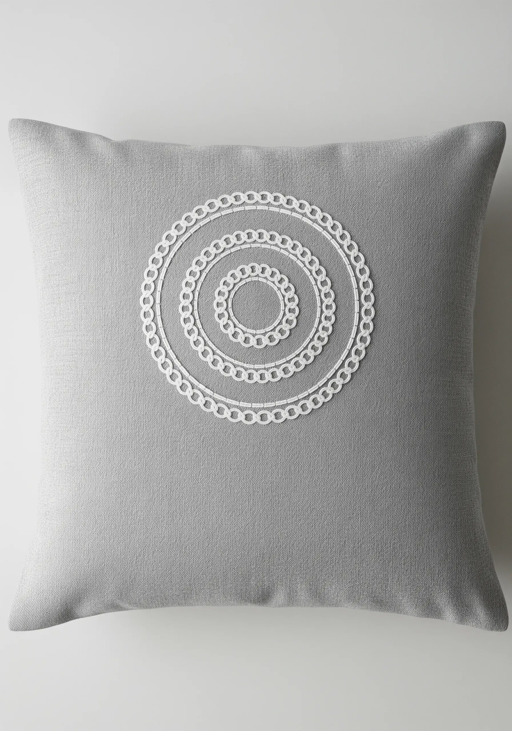 Concentric circles of white chain stitch embroidery on a grey pillow cover.