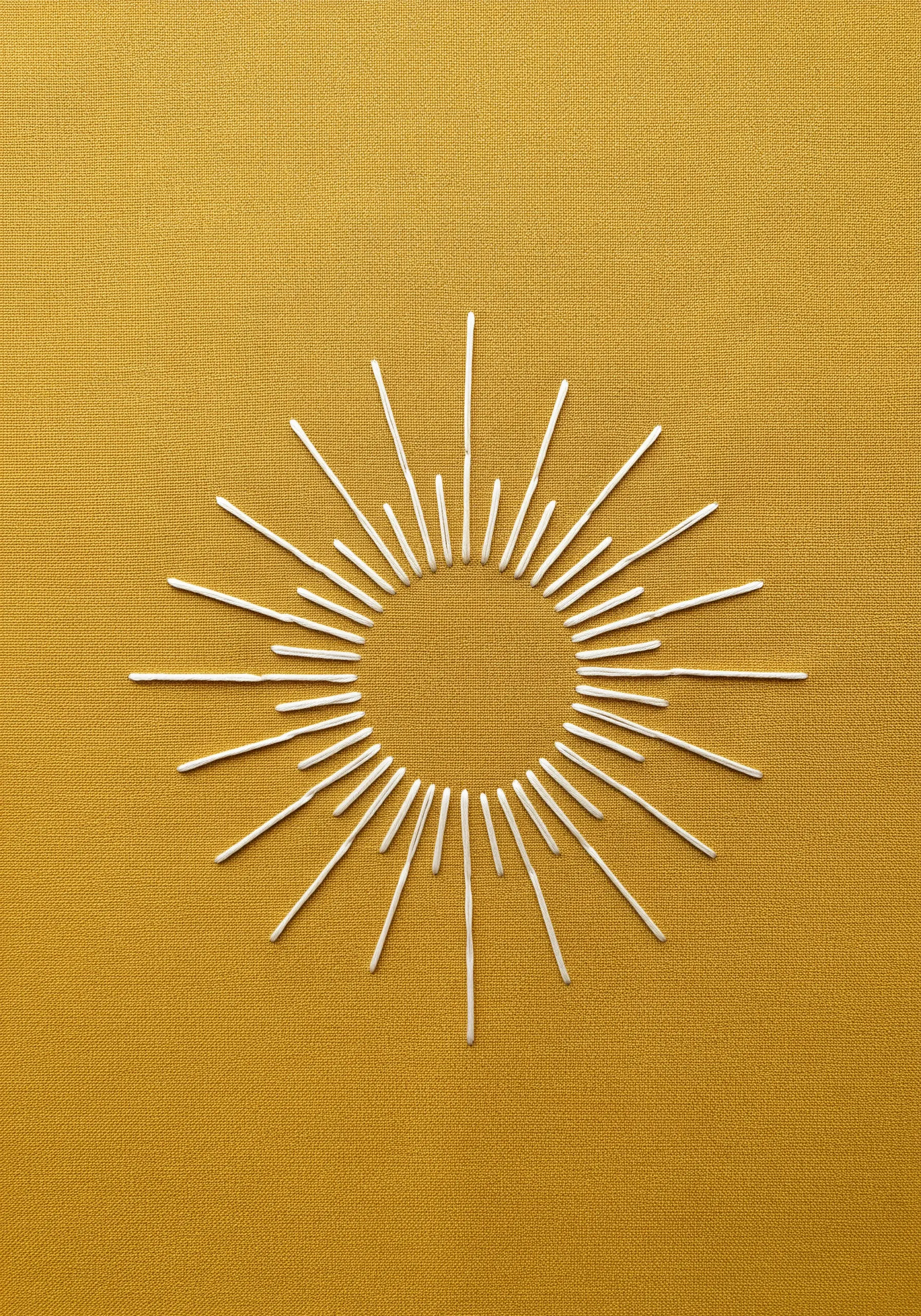 A sunburst motif made of white straight stitches radiating from an empty center.