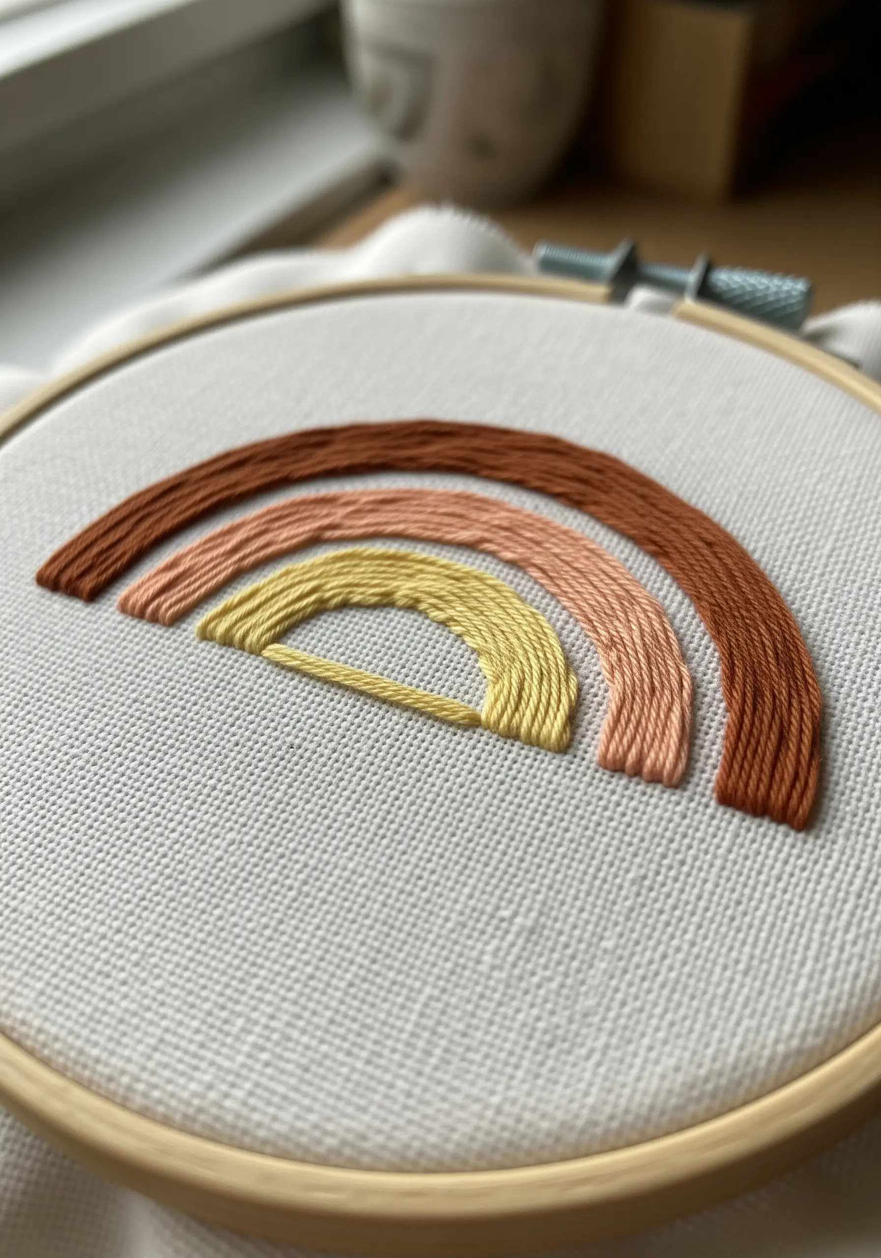 Close-up of a modern rainbow embroidered with a couching stitch in earthy tones.