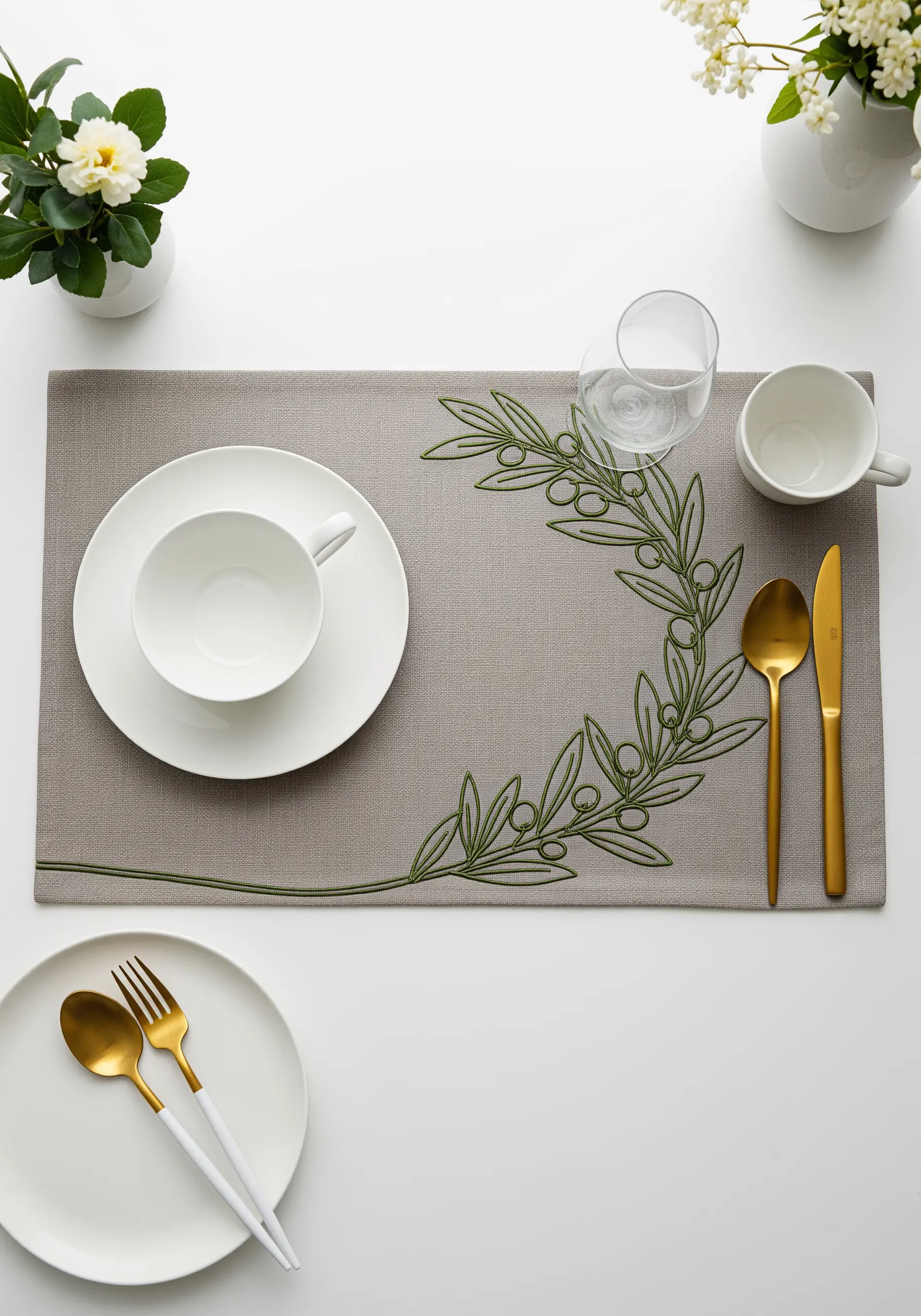 An olive branch motif embroidered in green thread to frame a grey linen placemat.