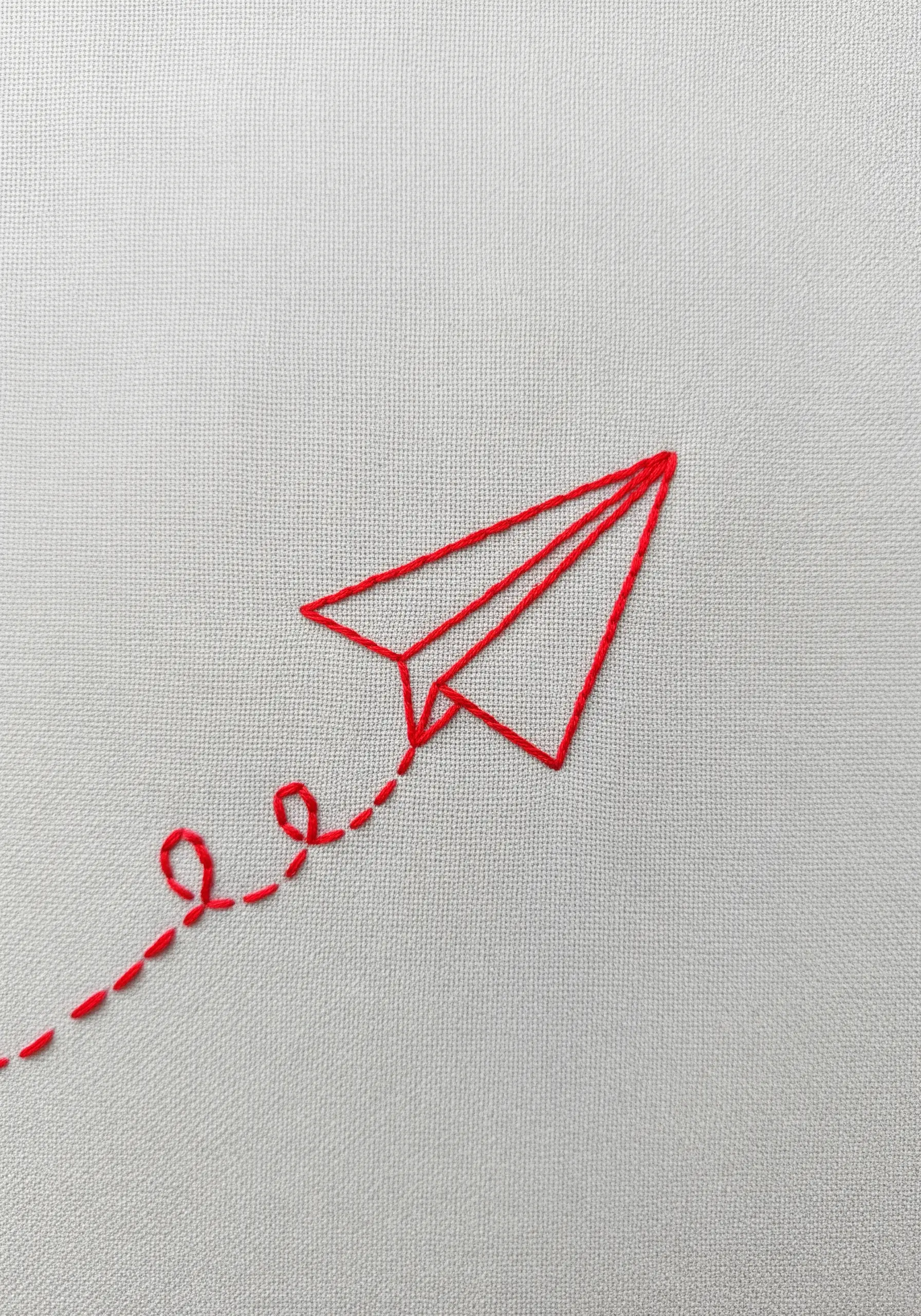 Minimalist red paper airplane embroidered with a trailing dotted line.
